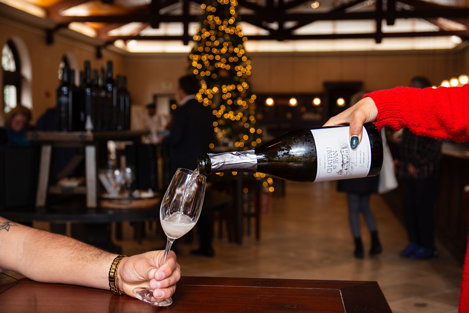 Red wine being poured into glass at festive restaurant with Christmas tree in background.