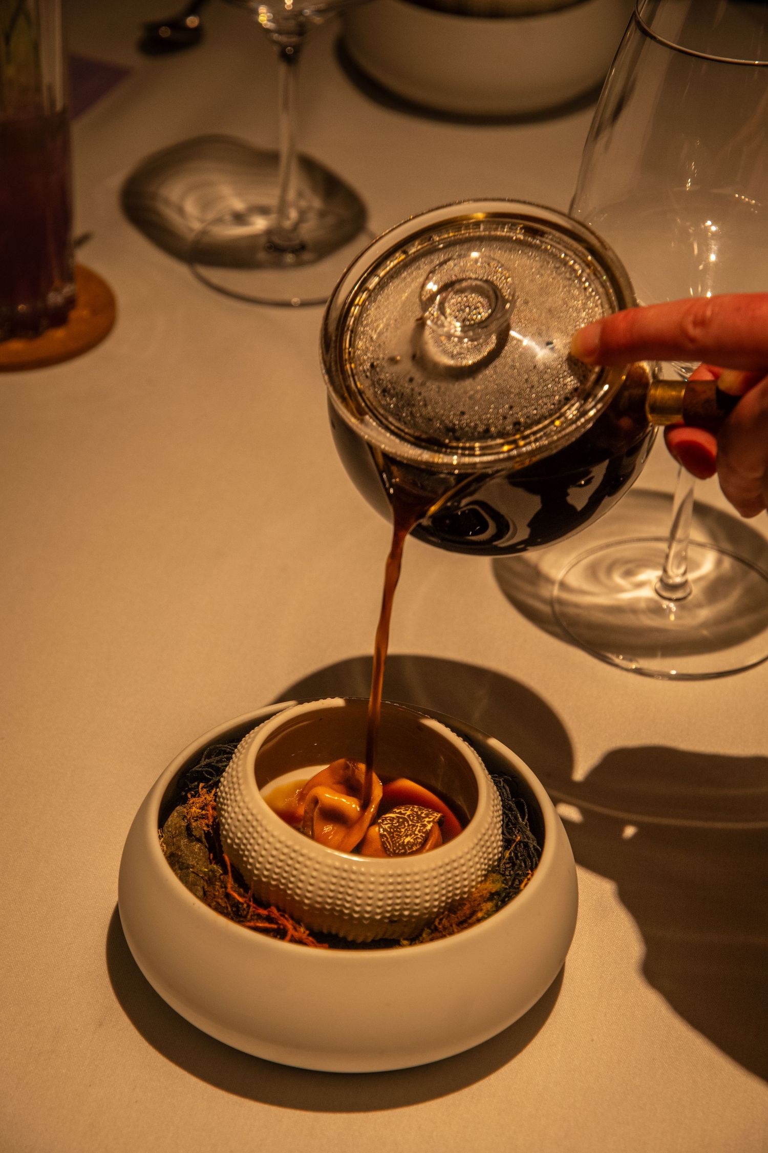 Close-up sequence of pouring dark liquid into elegant white ceramic dishes in a fine dining setting.