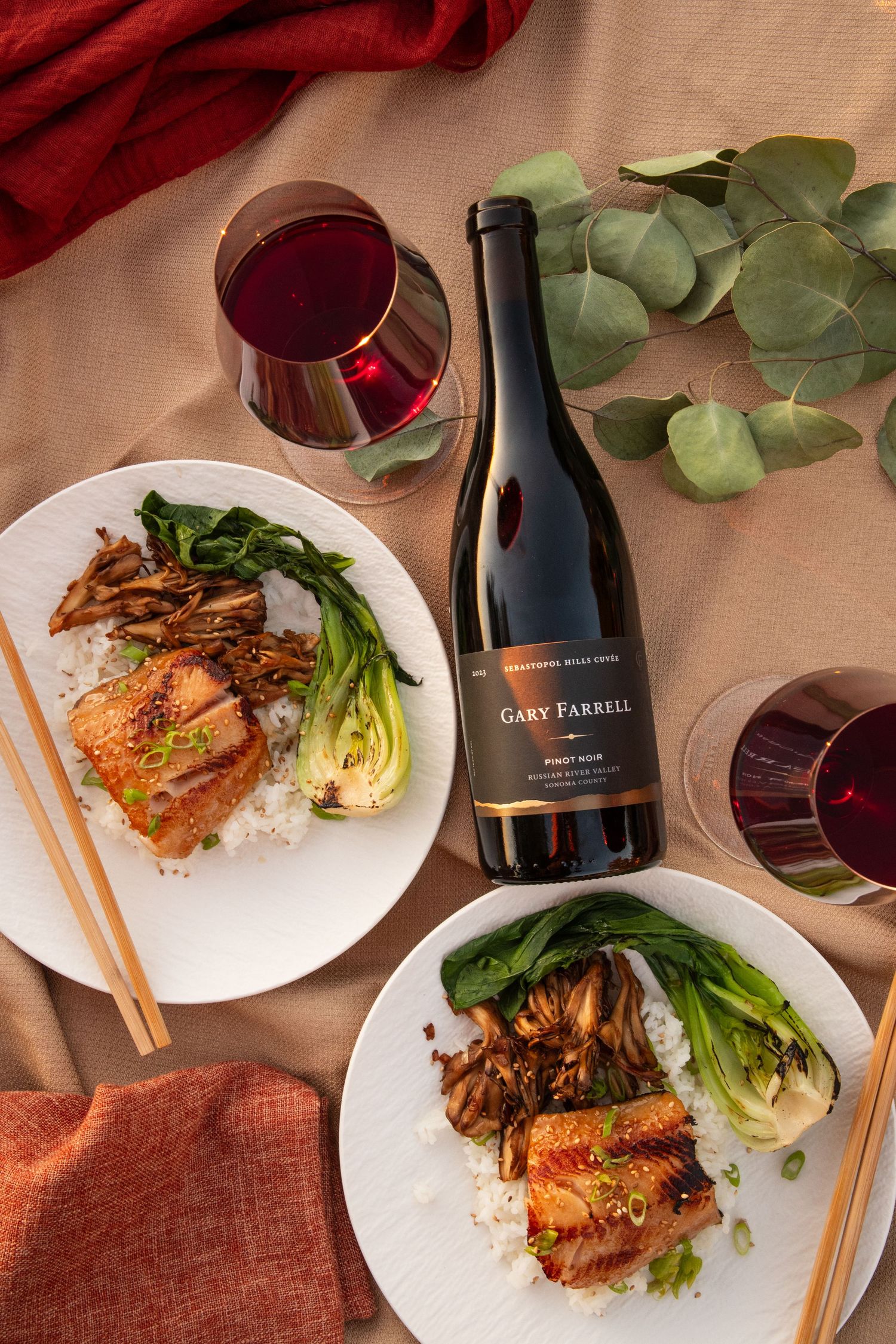 Elegant dinner setting with glazed salmon dishes and wine bottles on a rustic table.
