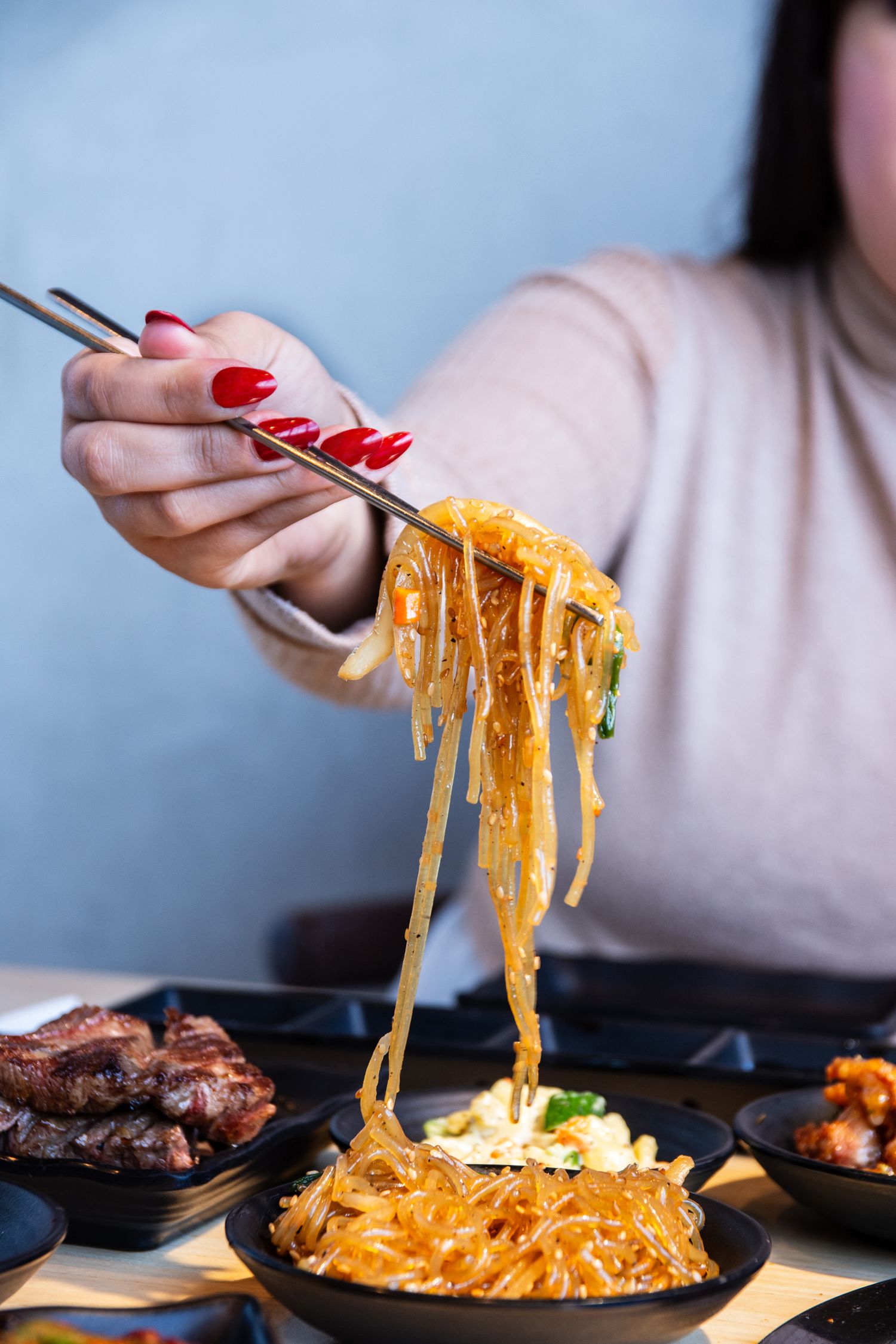 Stretchy cheese pull from a hot dish with chopsticks against a blue background.