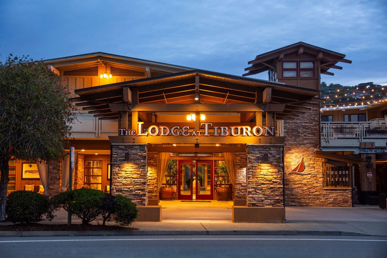 Exterior of Lodge at Tiburon hotel entrance lit up at dusk with stone and wood architecture.