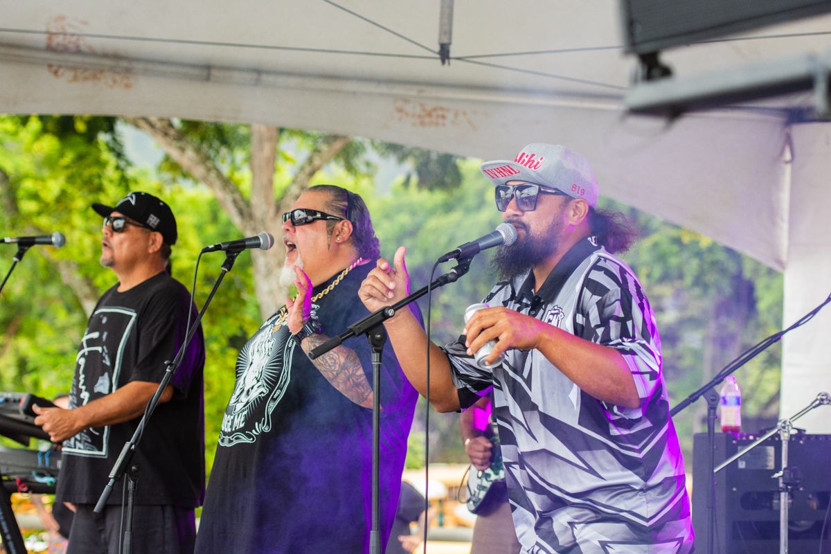 Band performs on outdoor stage with musicians singing into microphones.