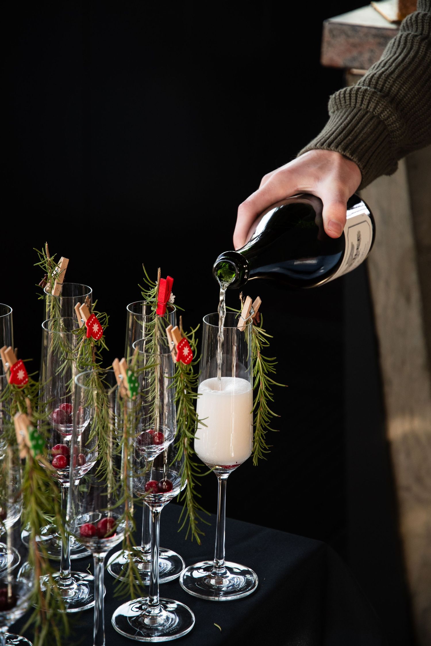 Champagne being poured into decorated flutes garnished with rosemary and berries.