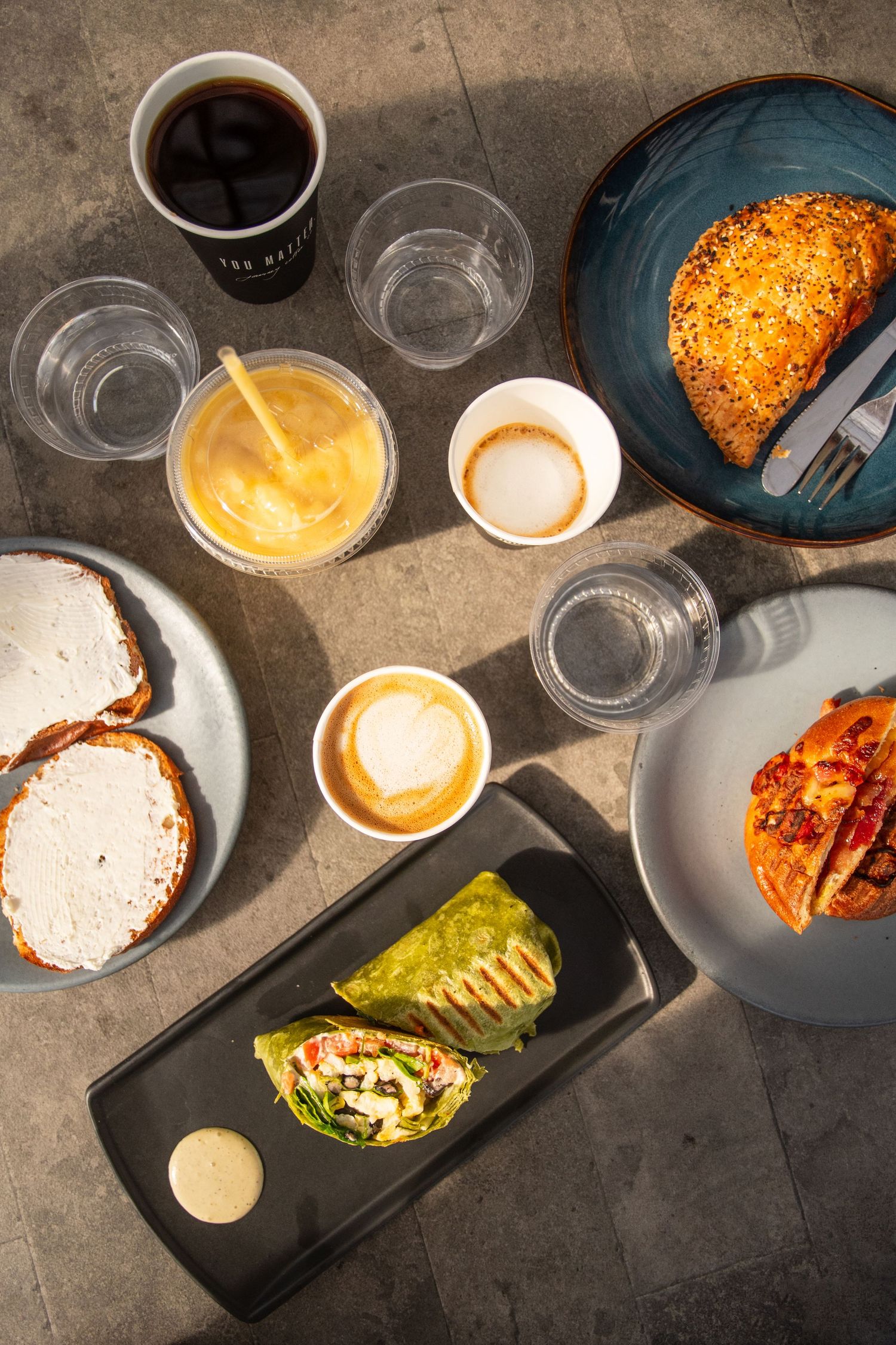 Overhead view of coffee drinks and food items arranged on a concrete surface at Journey Coffee Co.