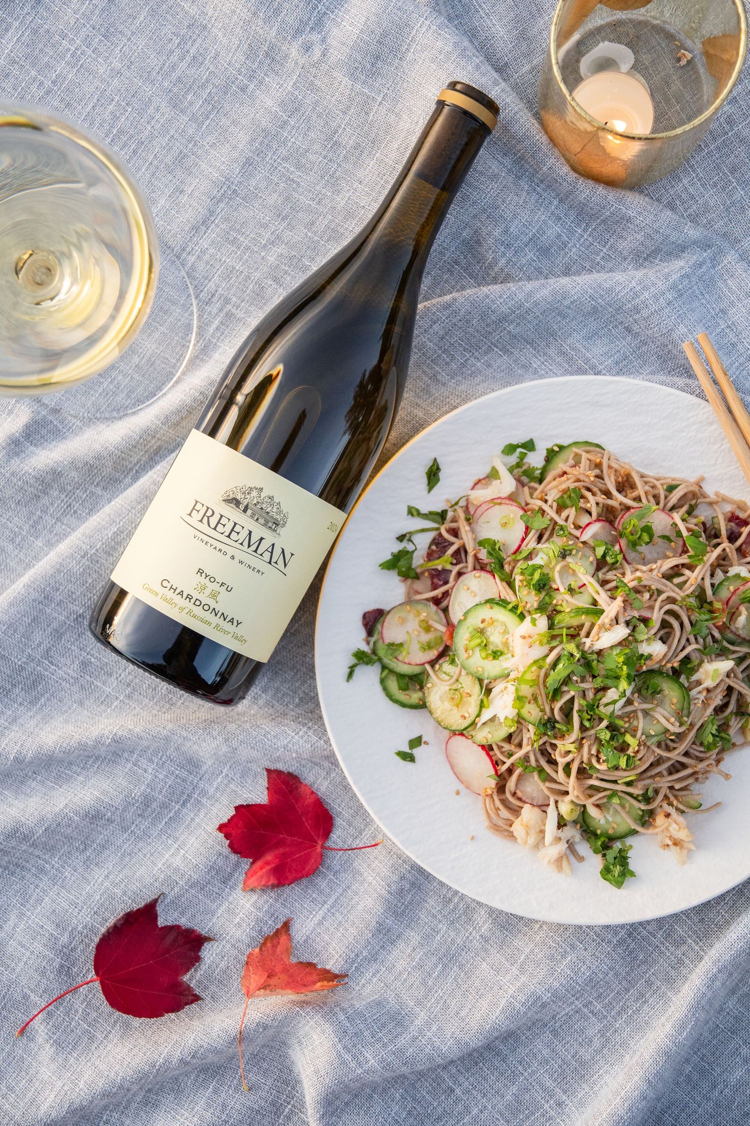 Asian noodle salad with red maple leaves and Freemark Abbey wine bottle on blue linen tablecloth.