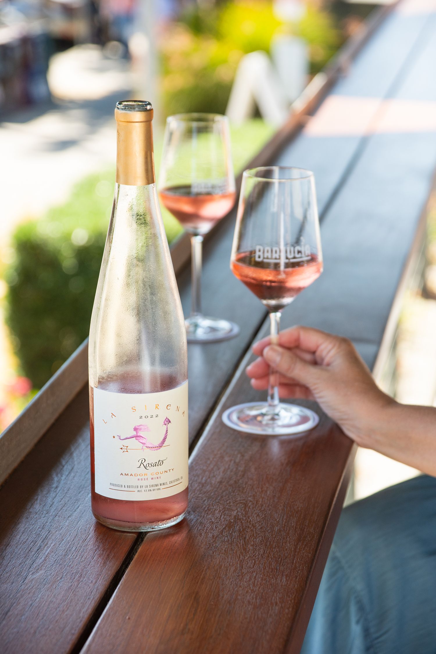 Rosé wine bottles and glasses arranged on wooden outdoor table.