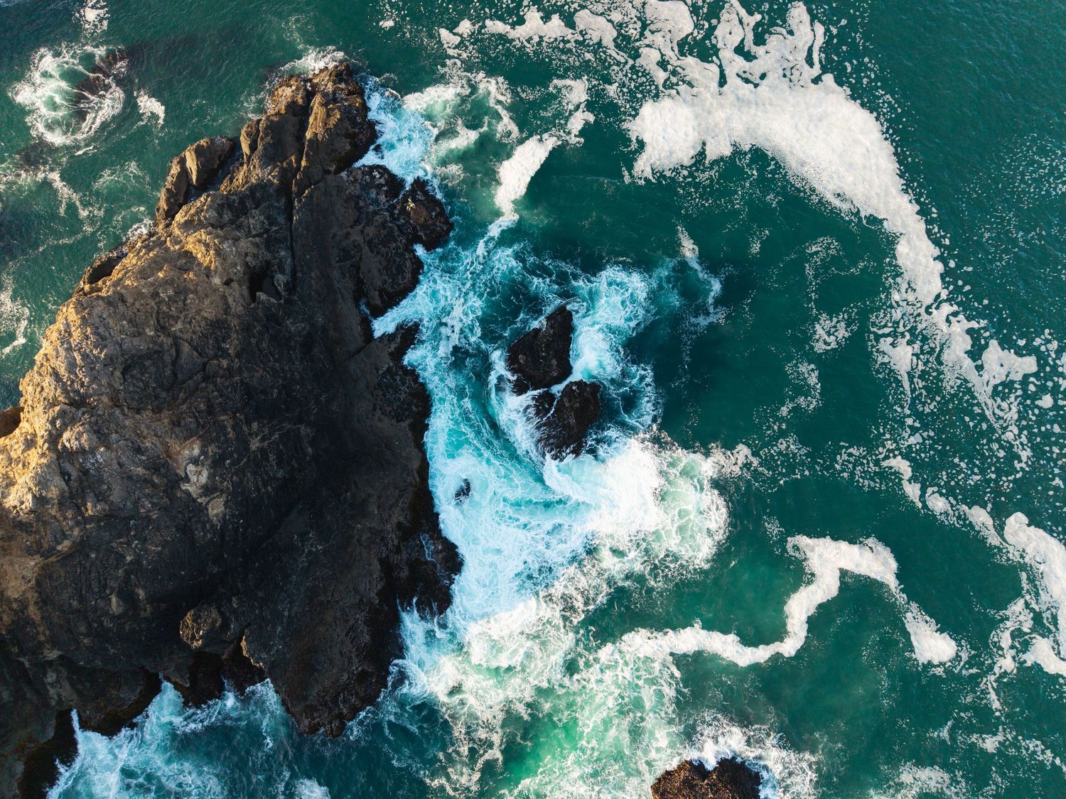 Aerial view of turquoise ocean waves crashing against rocky coastal cliffs.
