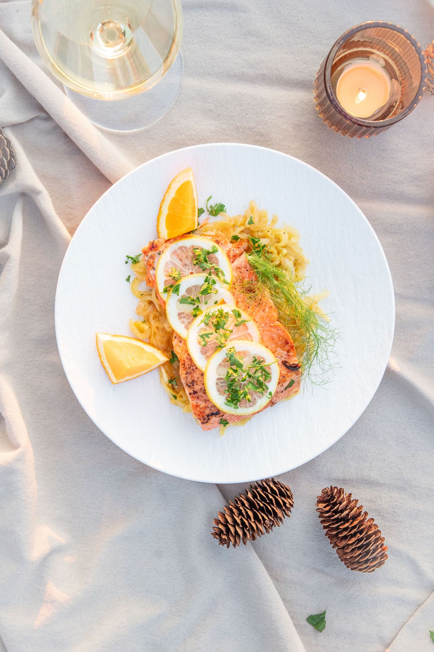 Elegant seafood dish with citrus garnish and fresh herbs served on white plates with pinecone decor.