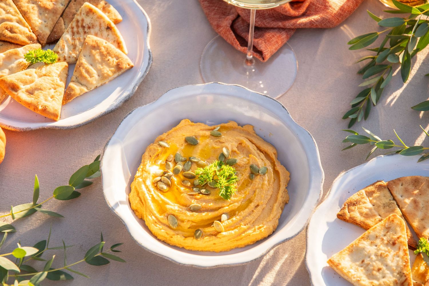 Creamy orange-colored dips garnished with herbs and olive oil in white serving bowls.