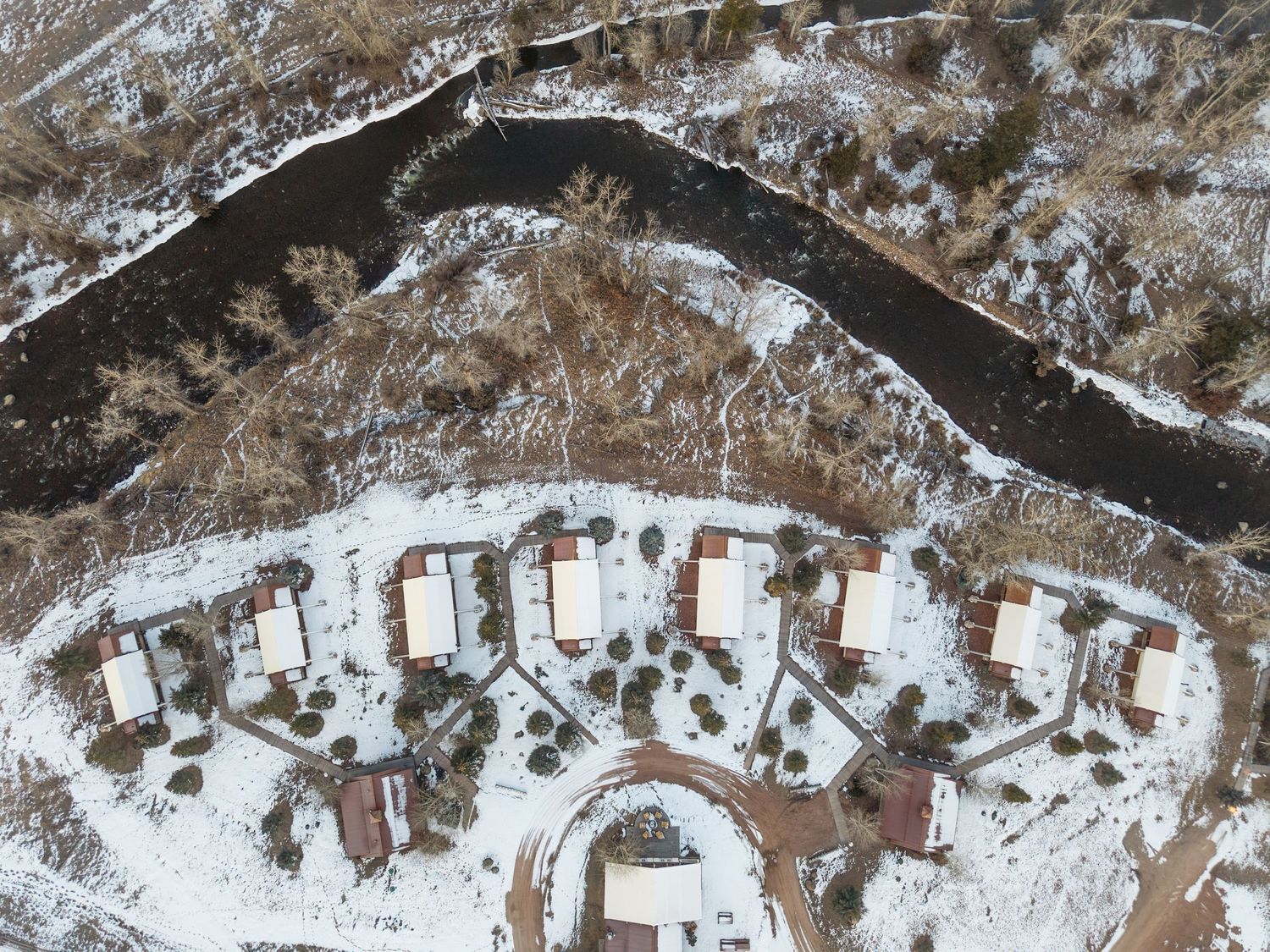 Aerial drone view of a snowy residential neighborhood with curved street near a dark river in winter.