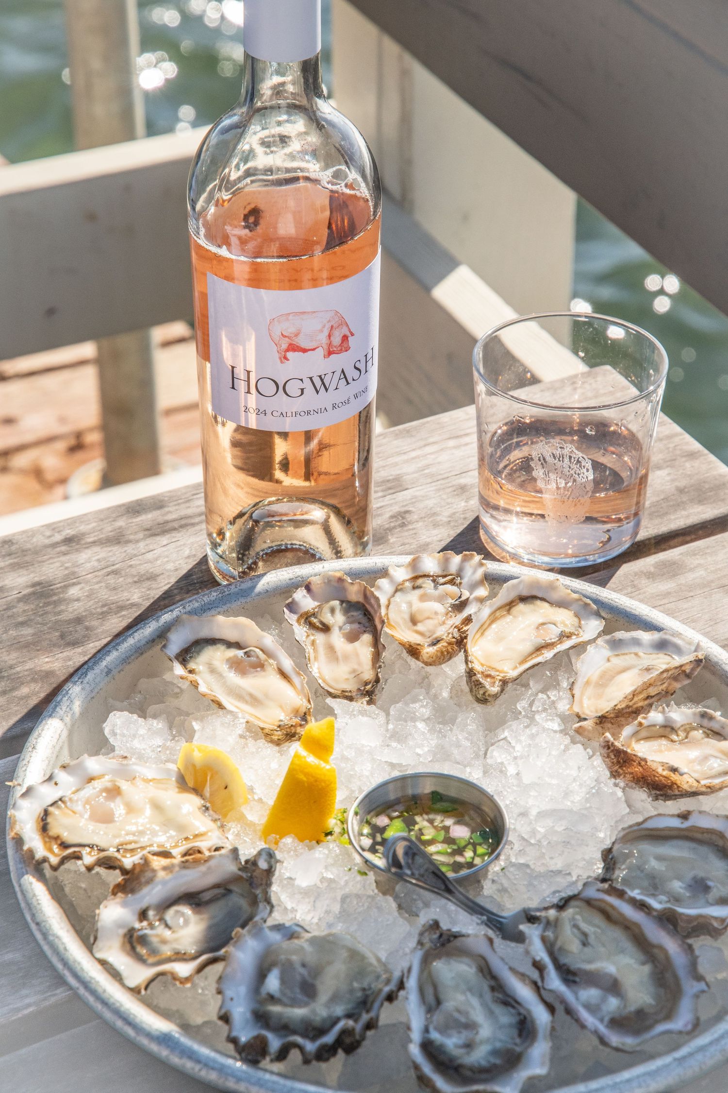 Rose wine bottle and fresh oysters on ice with lemon and mignonette sauce.