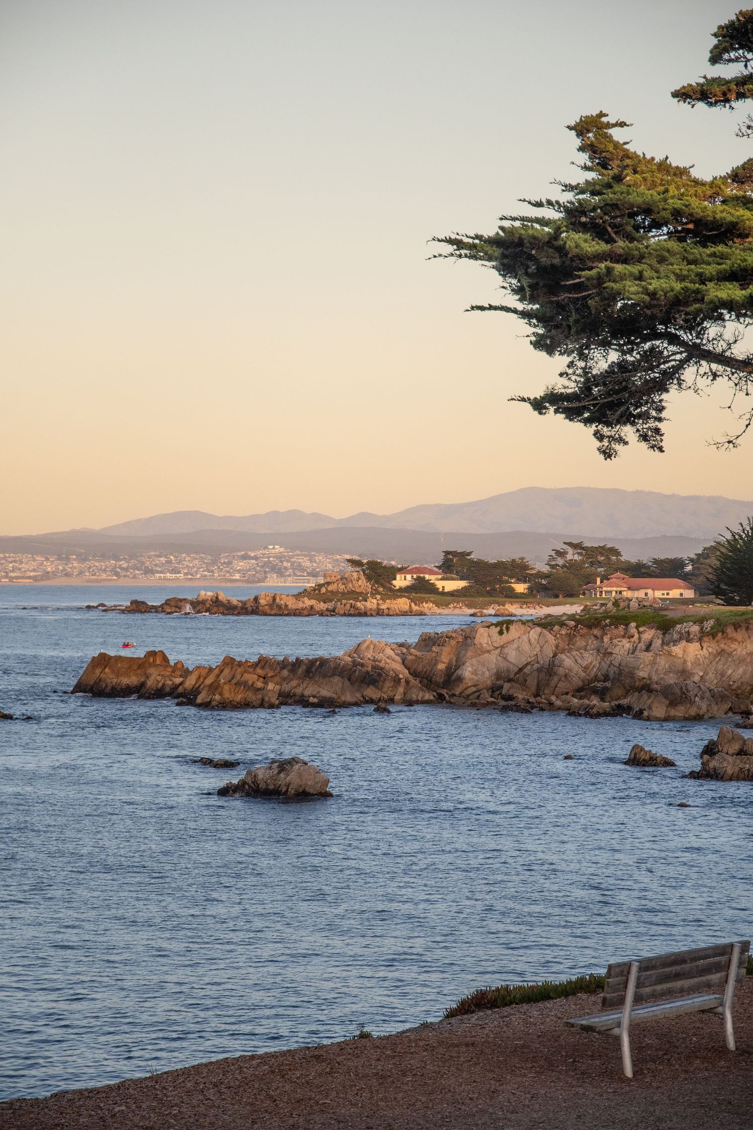 Scenic coastal view of rocky cliffs and ocean at sunset with mountains in background.