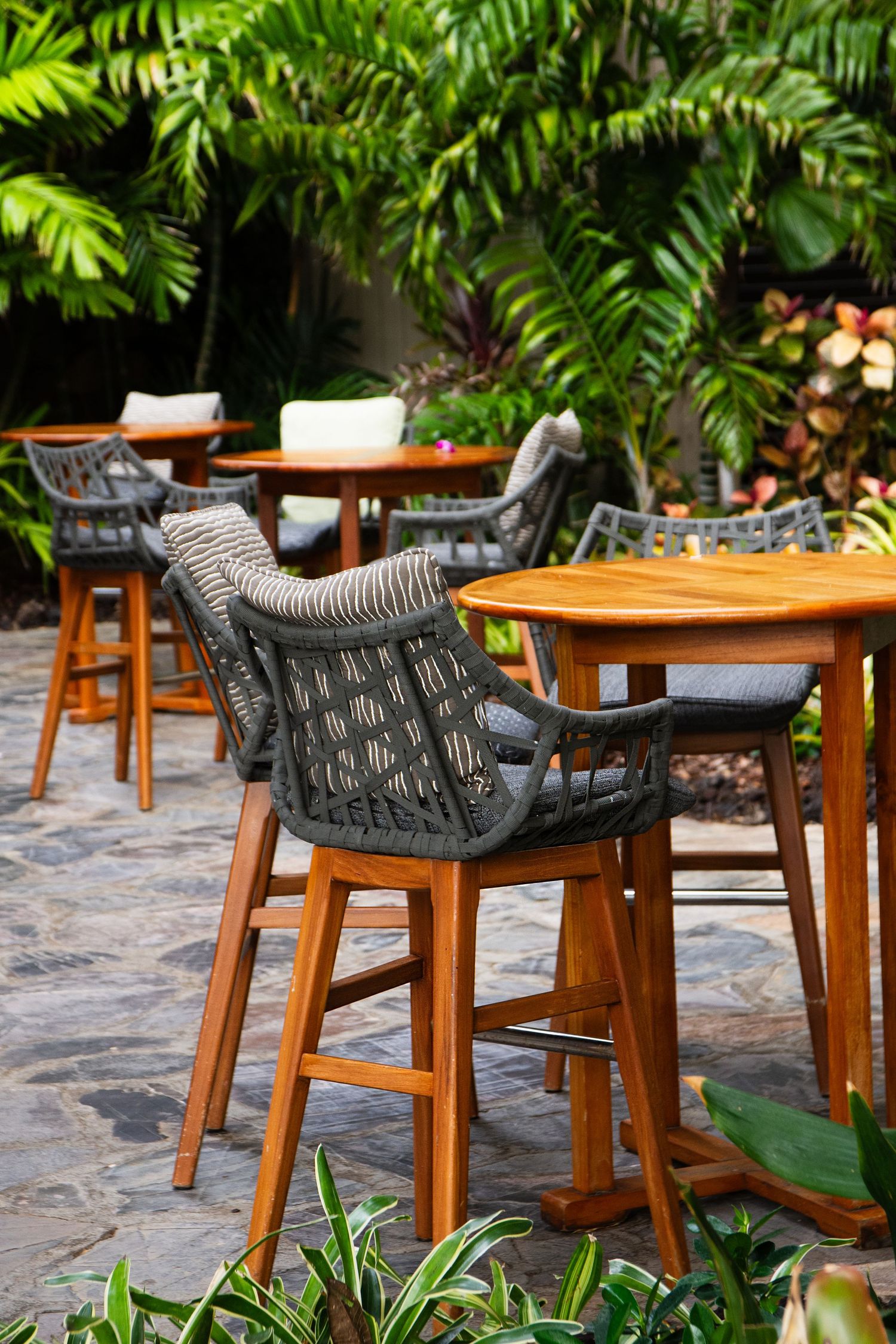 Outdoor dining area with modern bar stools and tropical foliage decor.