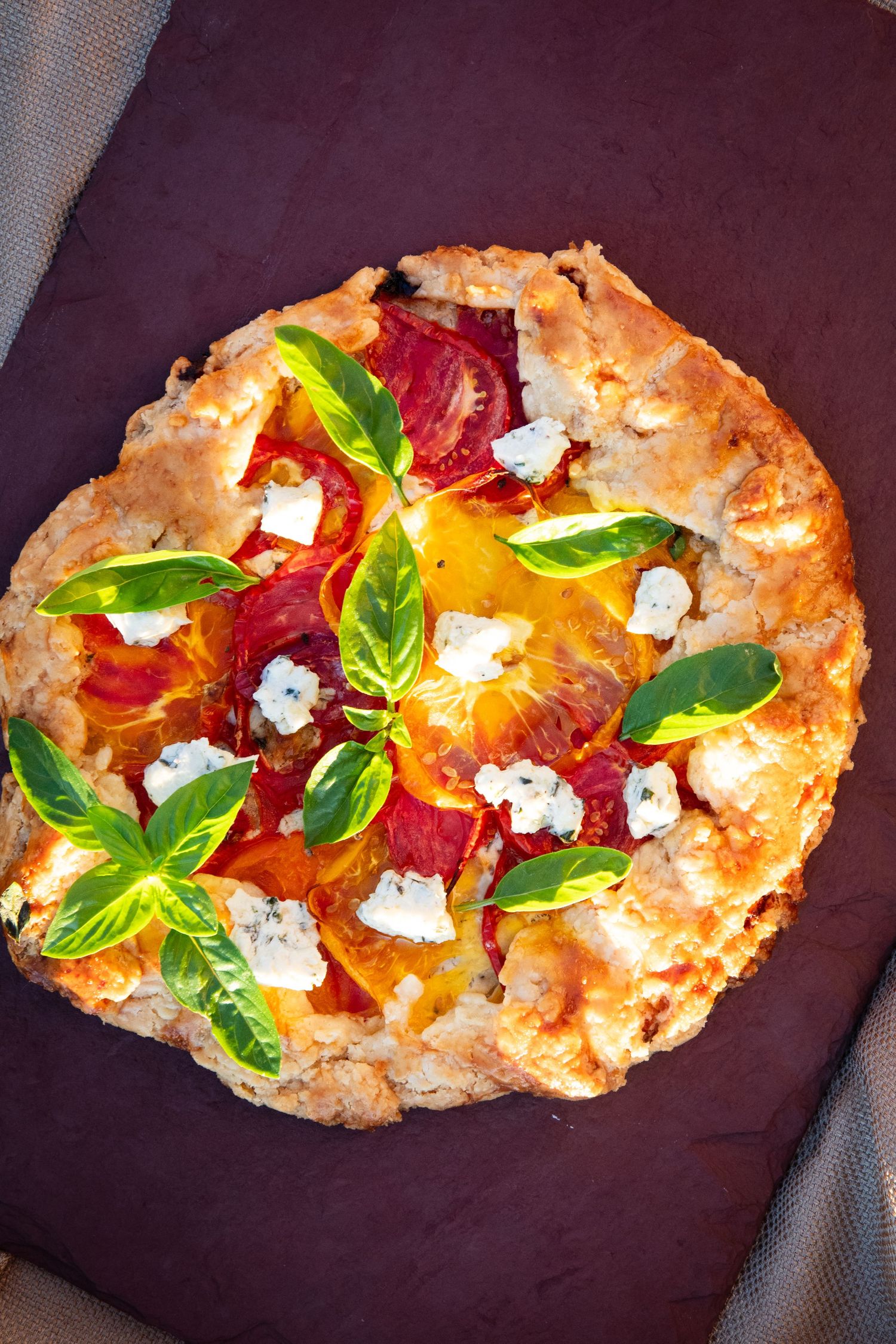 Artisanal flatbread topped with fresh basil, colorful citrus segments, and crumbled cheese on a dark background.