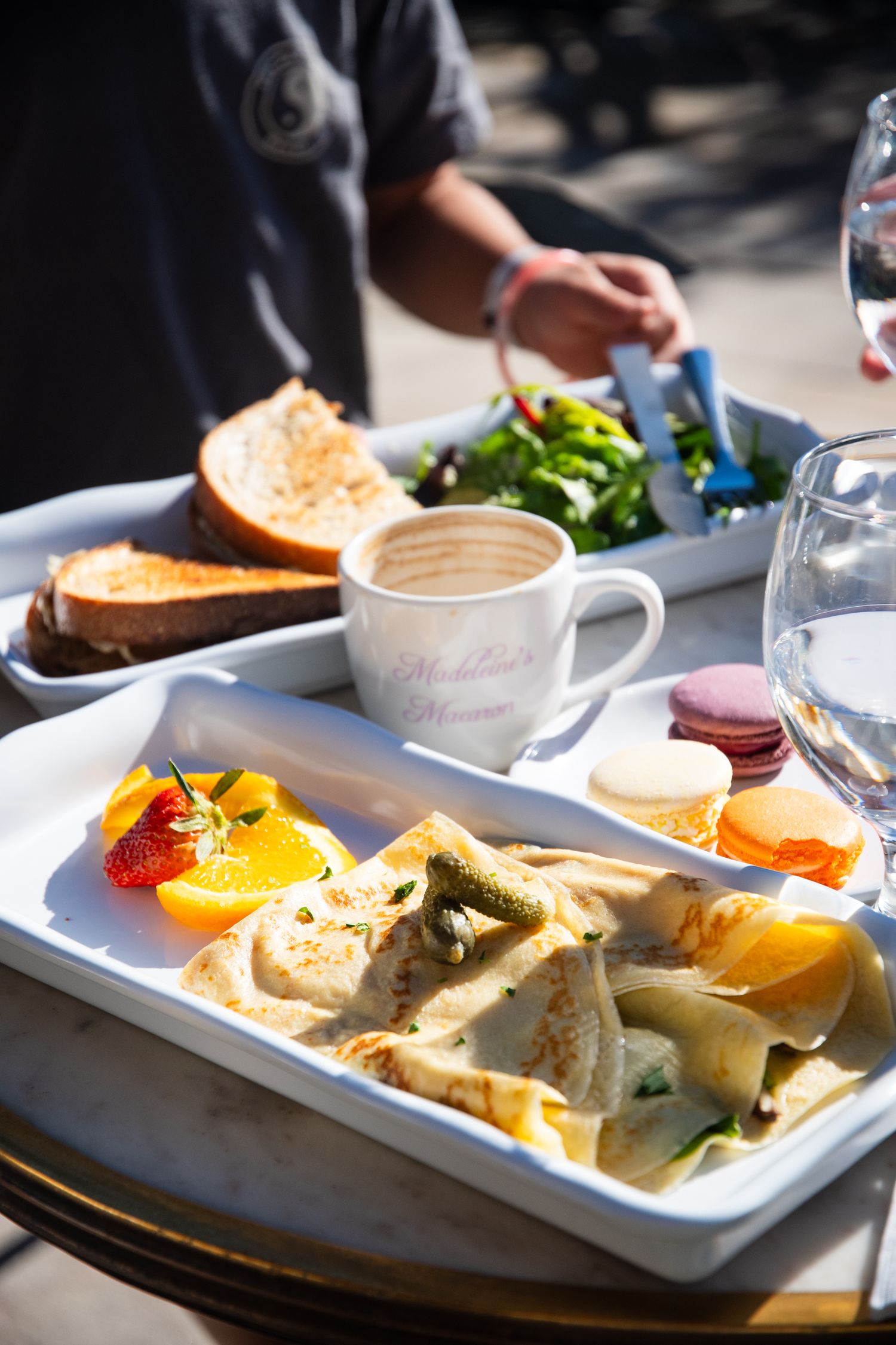Brunch spread featuring crepes, fresh fruit, coffee and macarons on white serving plates.