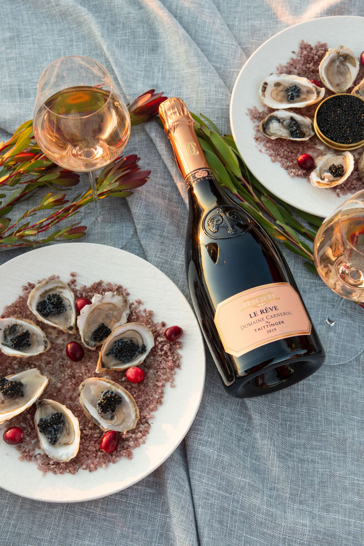 Champagne and oysters with caviar served on a gray tablecloth with decorative garnishes.
