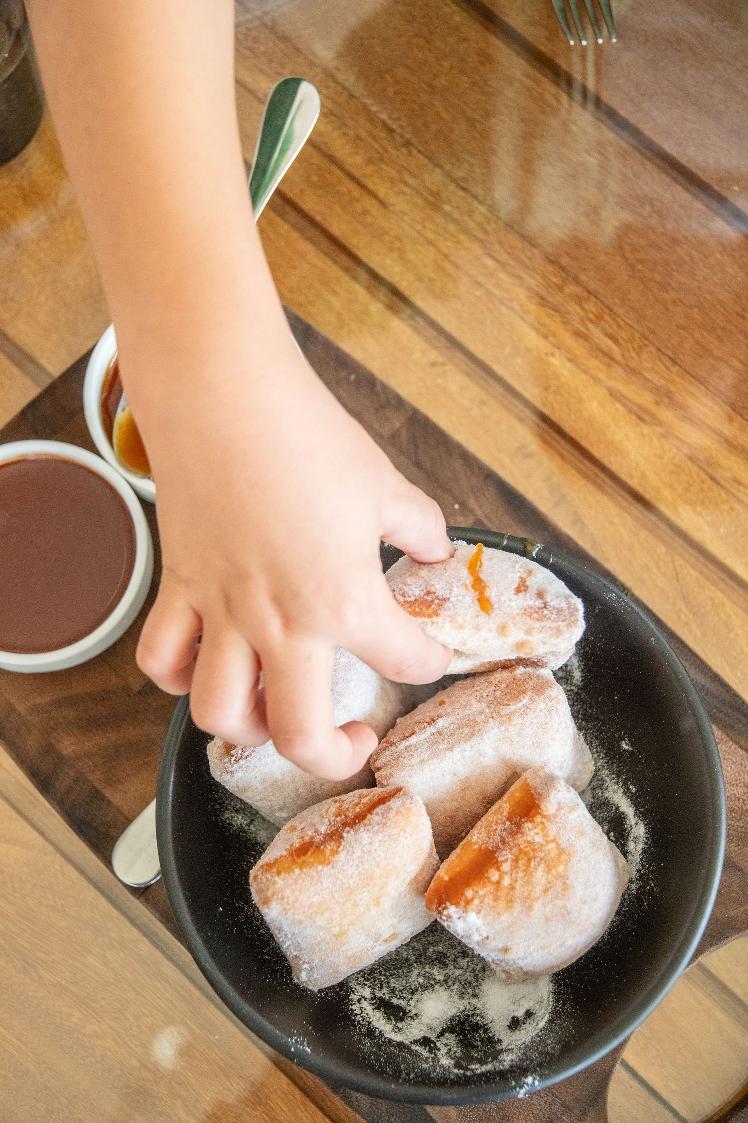 Hand sprinkling powdered sugar over freshly baked pastries on a dark plate.