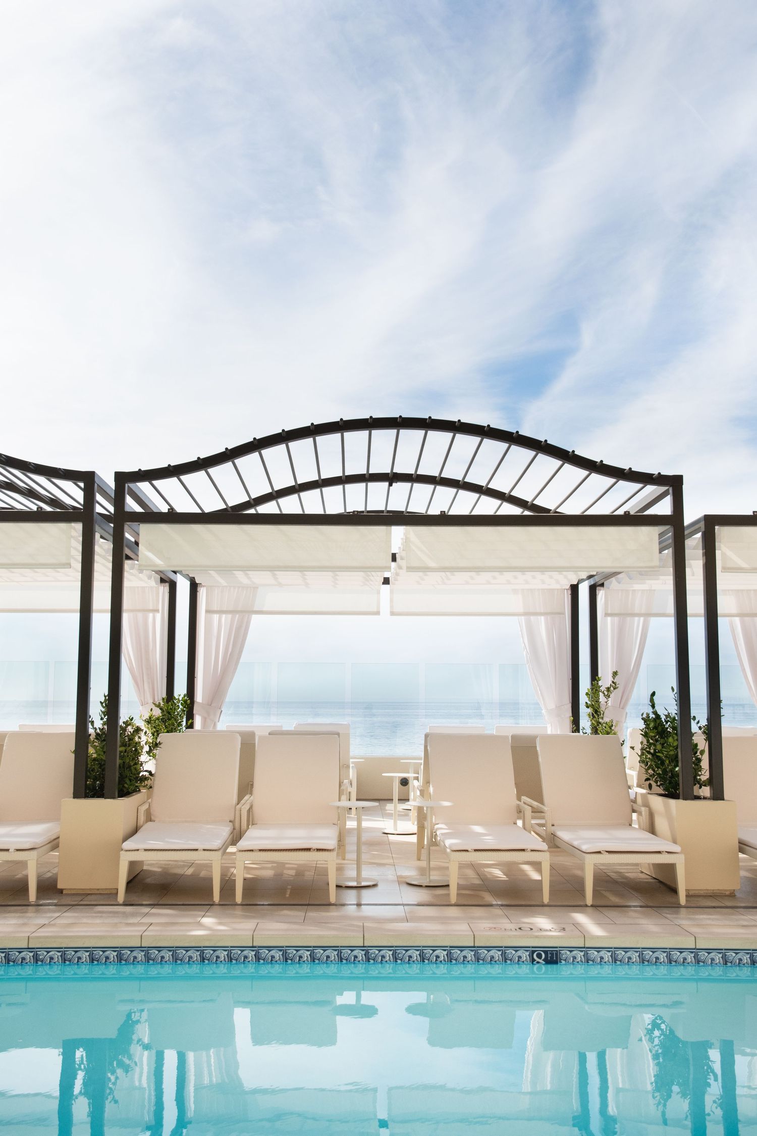 Elegant poolside lounge area with white cabanas and turquoise water under a covered pergola.