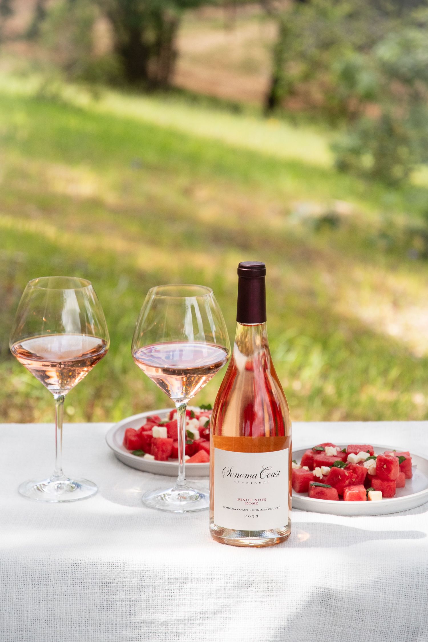 Table setting with rosé wine glasses and fresh strawberries on white linen.