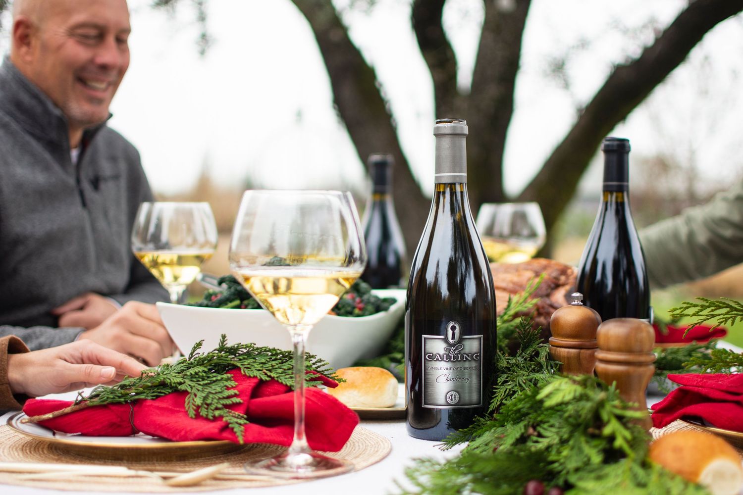 Wine bottles and glasses arranged on a rustic outdoor table with fresh greenery and natural decor.