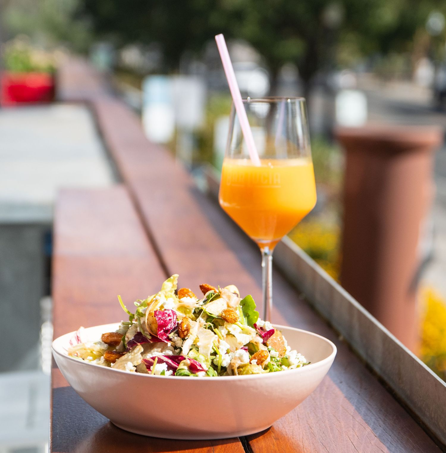 Fresh salad bowl and orange cocktail served on outdoor dining table.