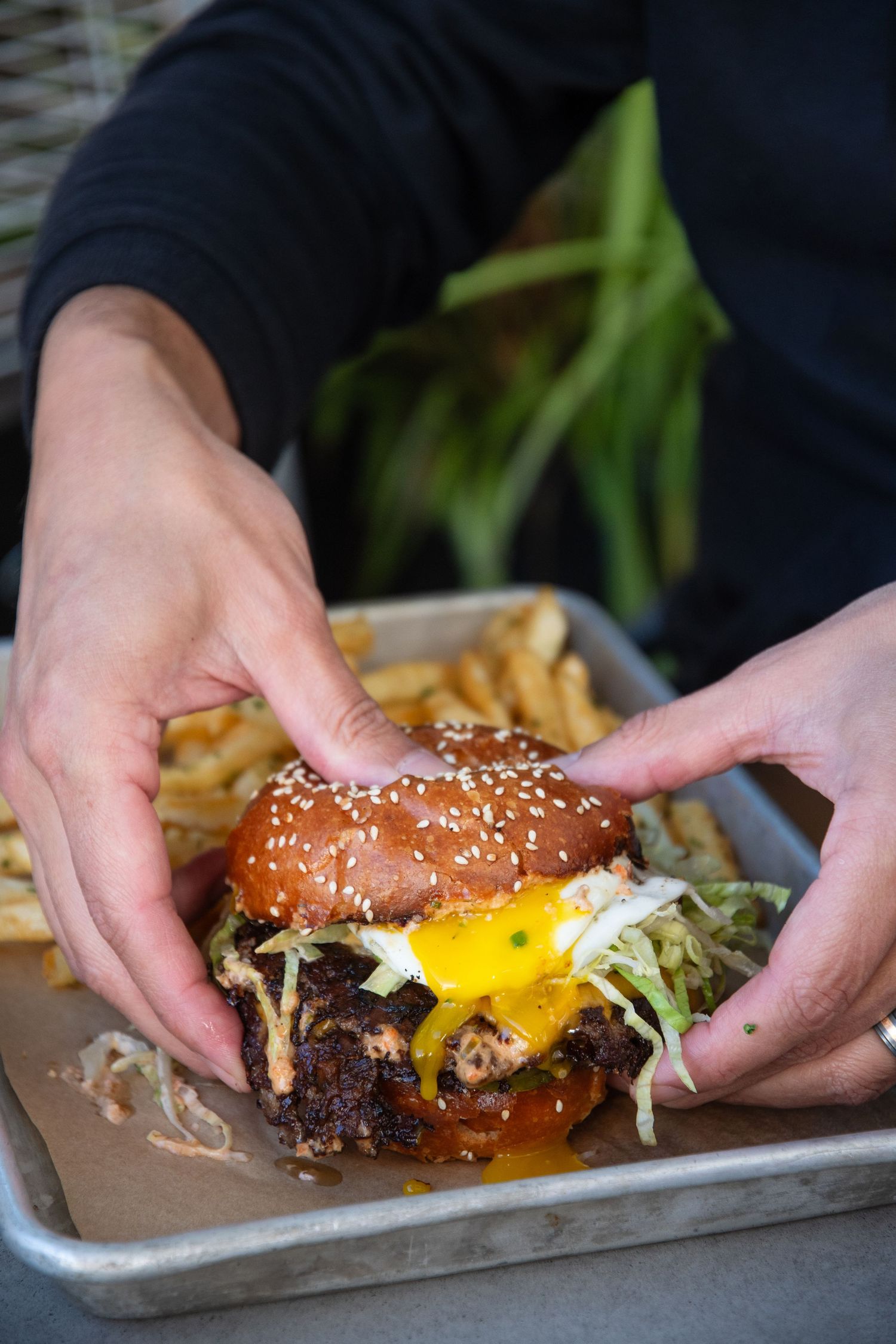 Gourmet burger with melted cheese and sesame bun being served on a metal tray.