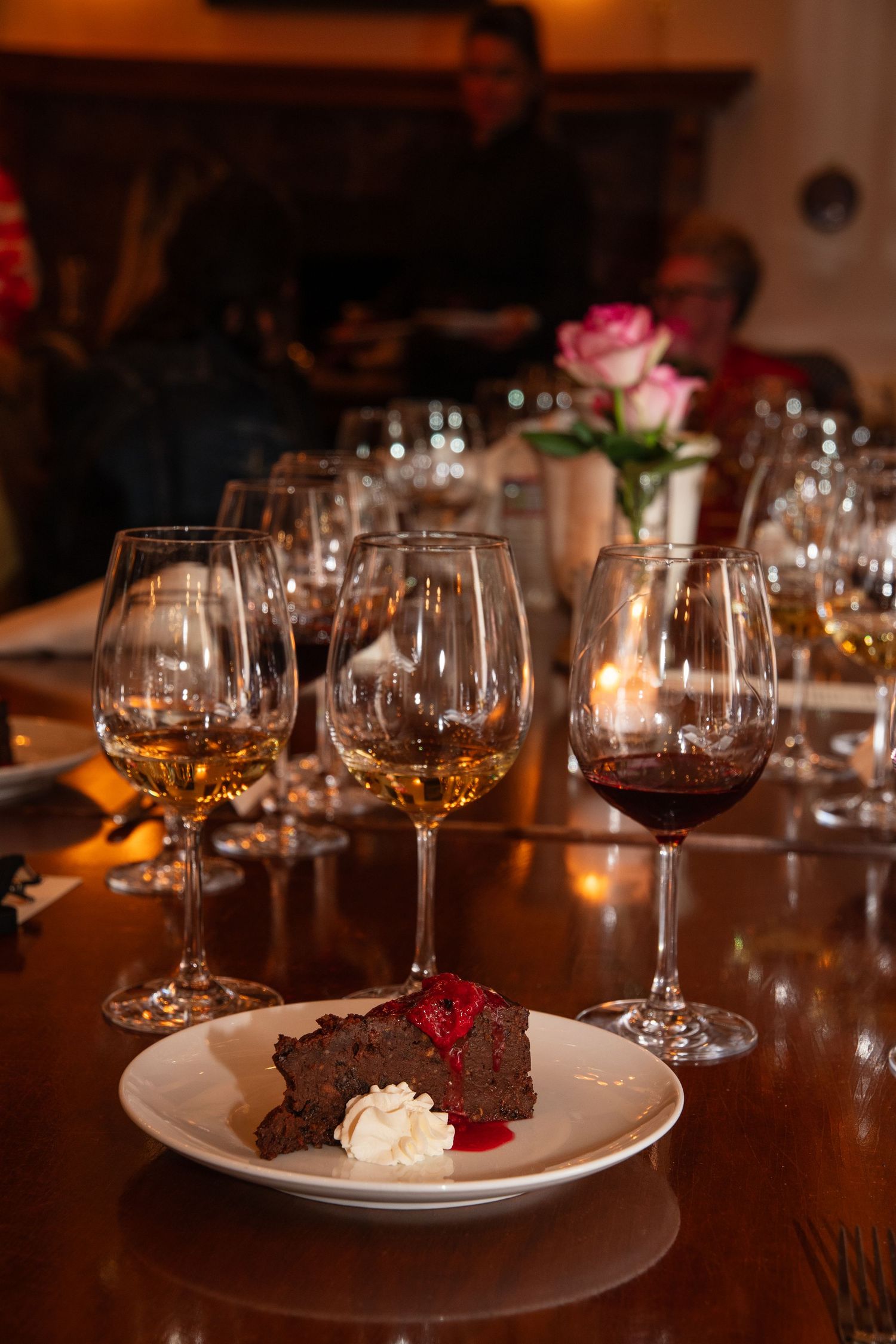 Wine glasses and chocolate cake with whipped cream on a dark wooden table in intimate lighting.