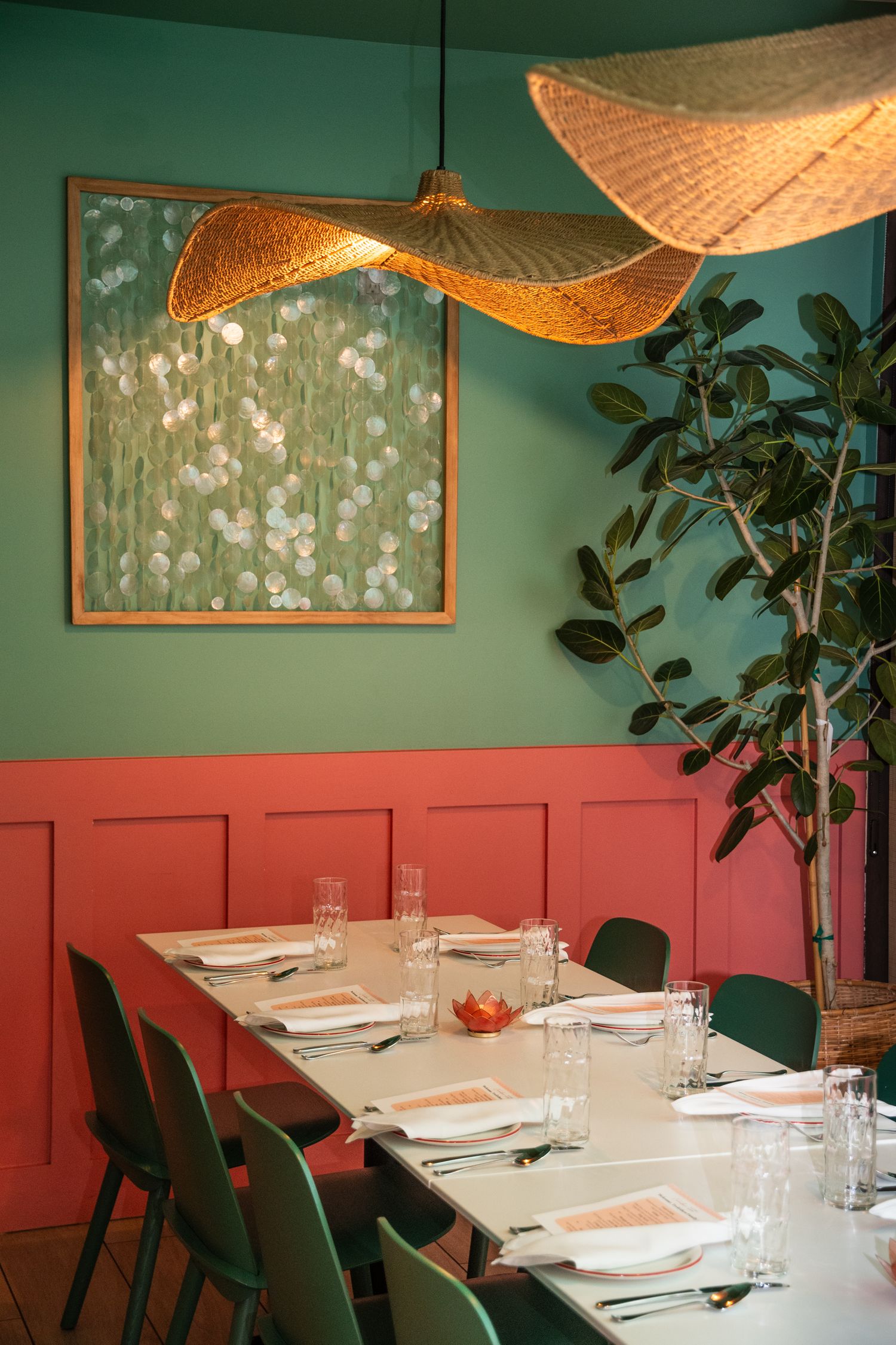 Modern restaurant dining room with teal walls, coral wainscoting, and woven pendant lights.
