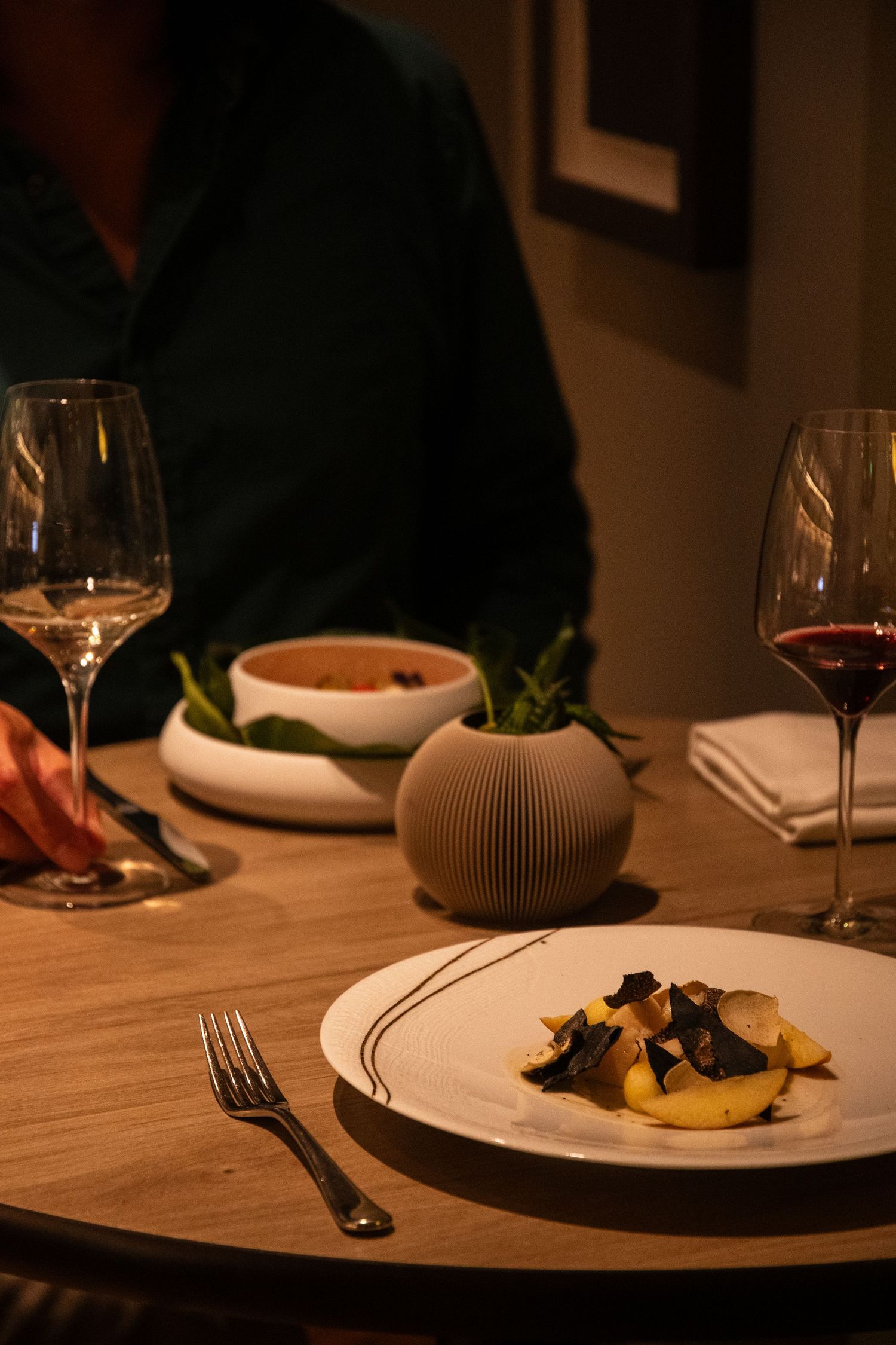 Elegant plated dishes on a wooden table with wine glasses and modern table settings in warm lighting.