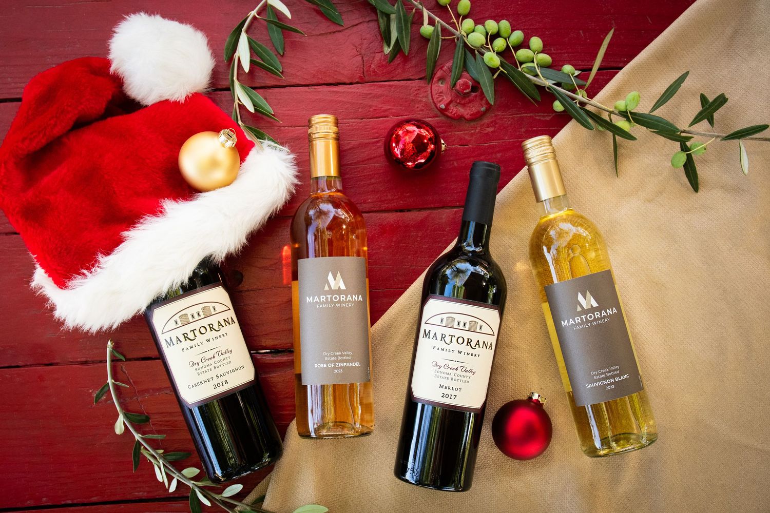 Holiday-themed wine bottle display on red wood with Santa hat and festive decorations.