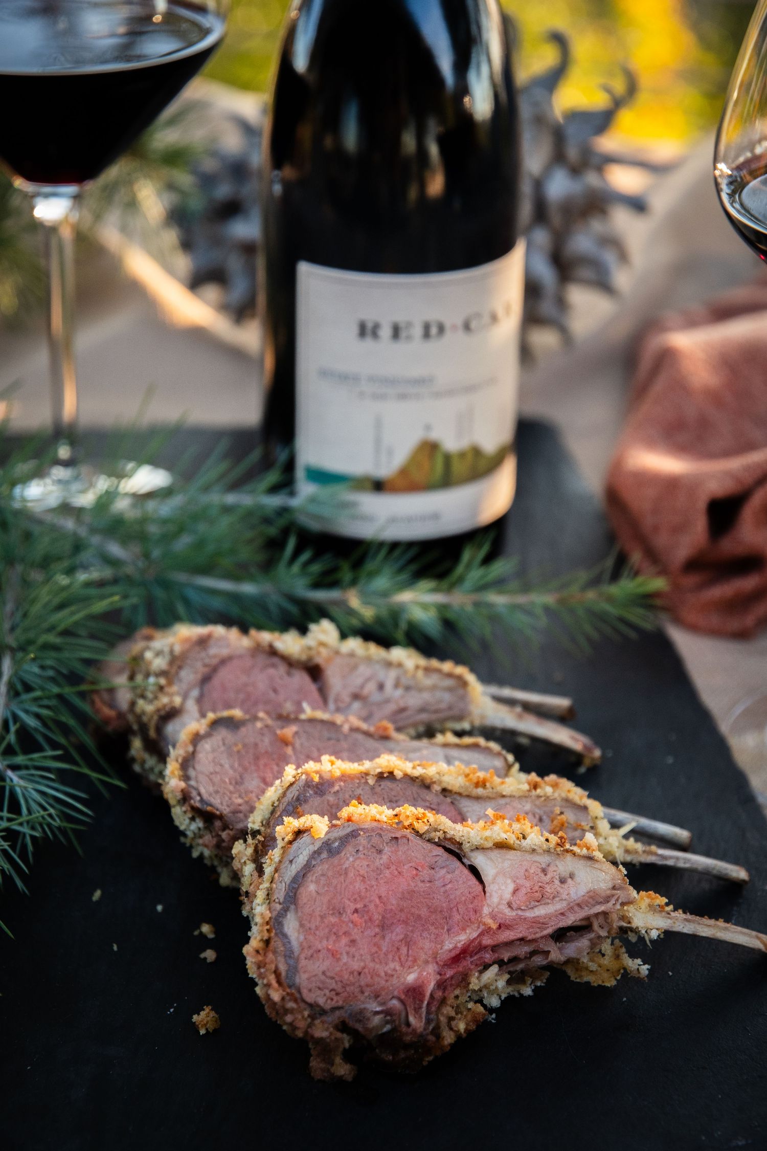 Sliced rare beef roast displayed with wine bottles and evergreen garnish.