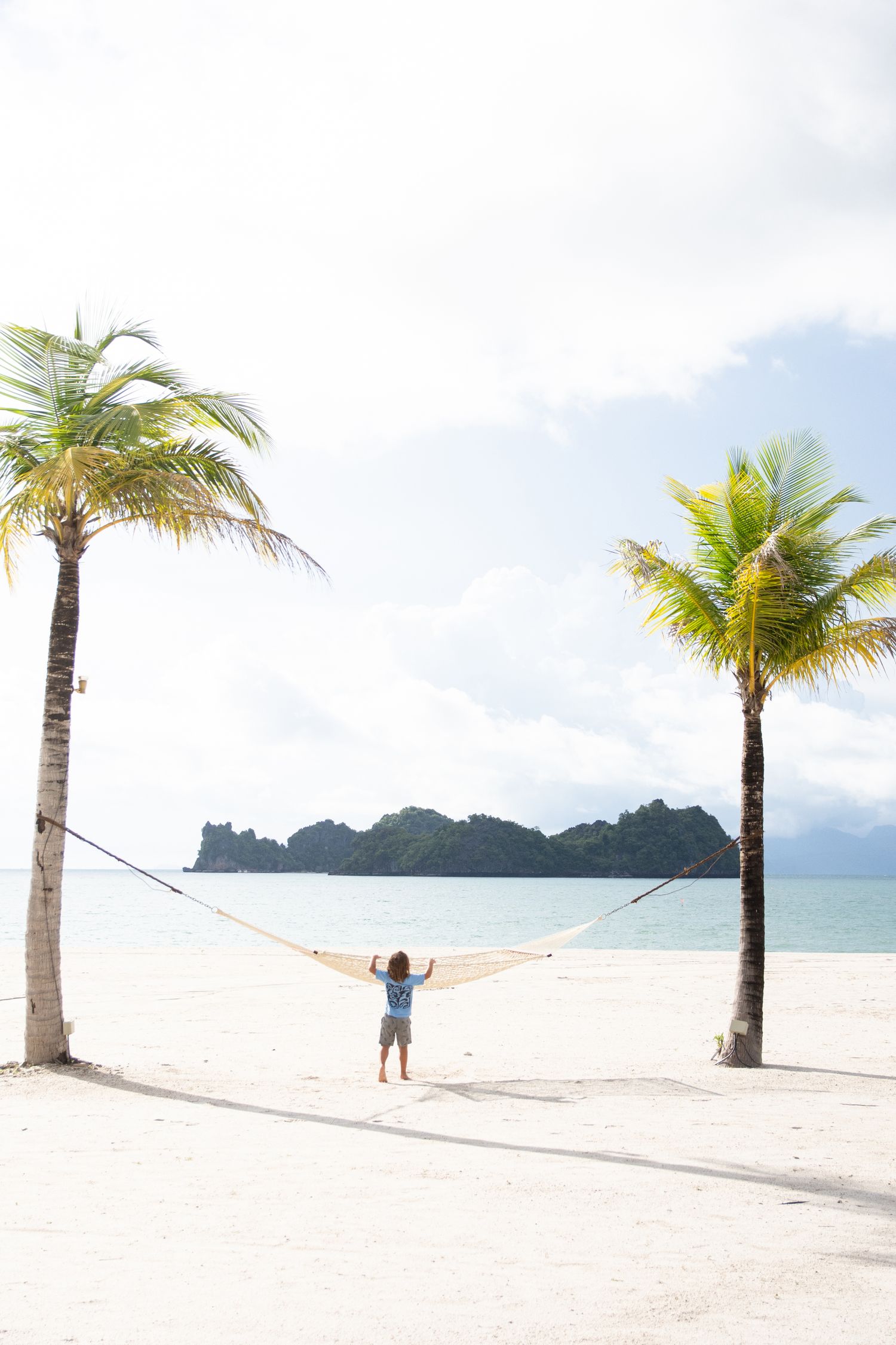 Palm trees and hammock on a pristine white sand beach with mountains in the distance.