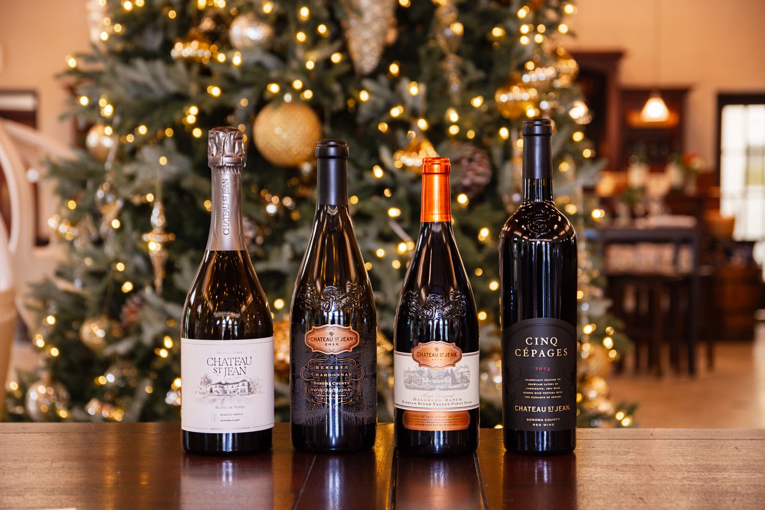 Four wine bottles displayed in front of decorated Christmas tree in tasting room.