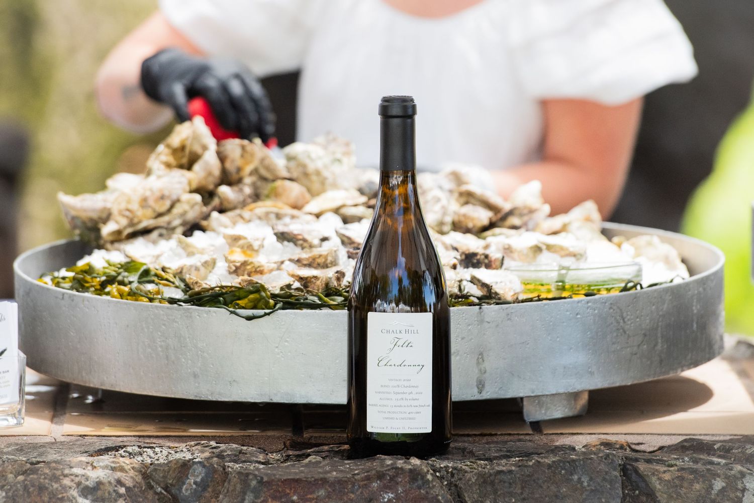 Overhead view of a rustic outdoor dining table with wine bottles and platters of food.