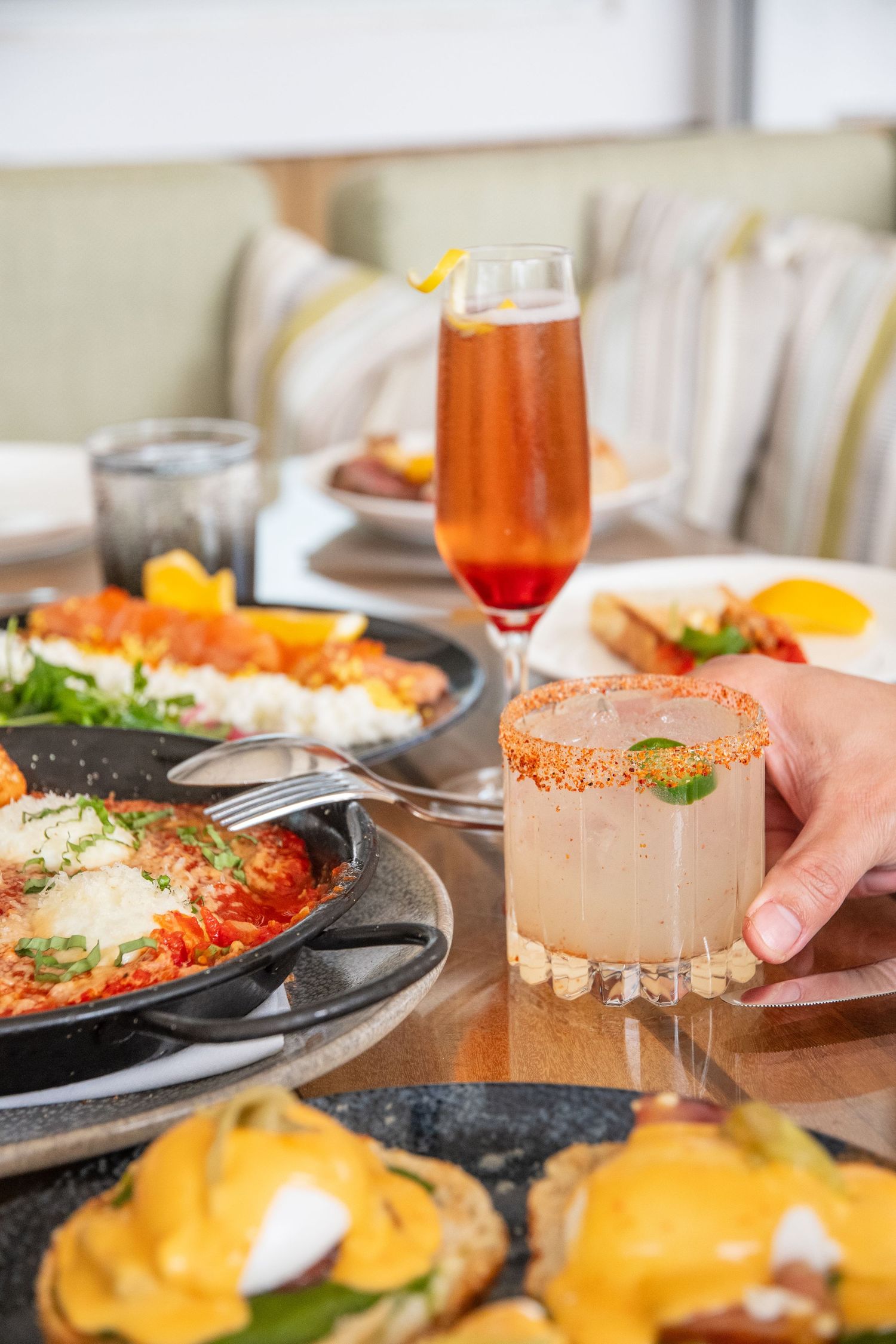 Brunch spread with eggs benedict, cocktails and garnished drinks on restaurant table.