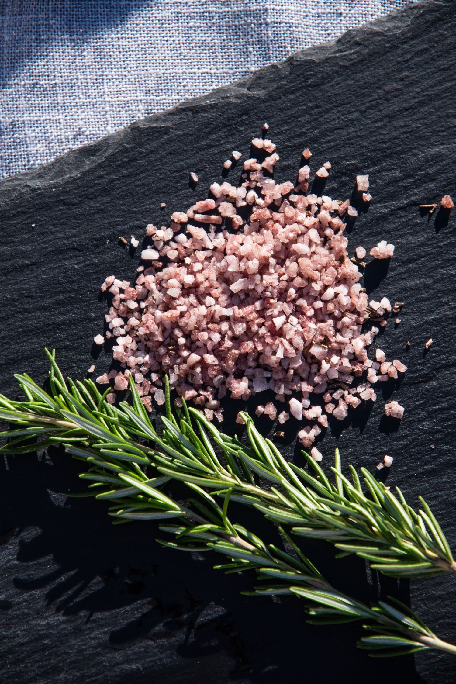 Pink Himalayan salt crystals and fresh rosemary sprig arranged on black stone background.