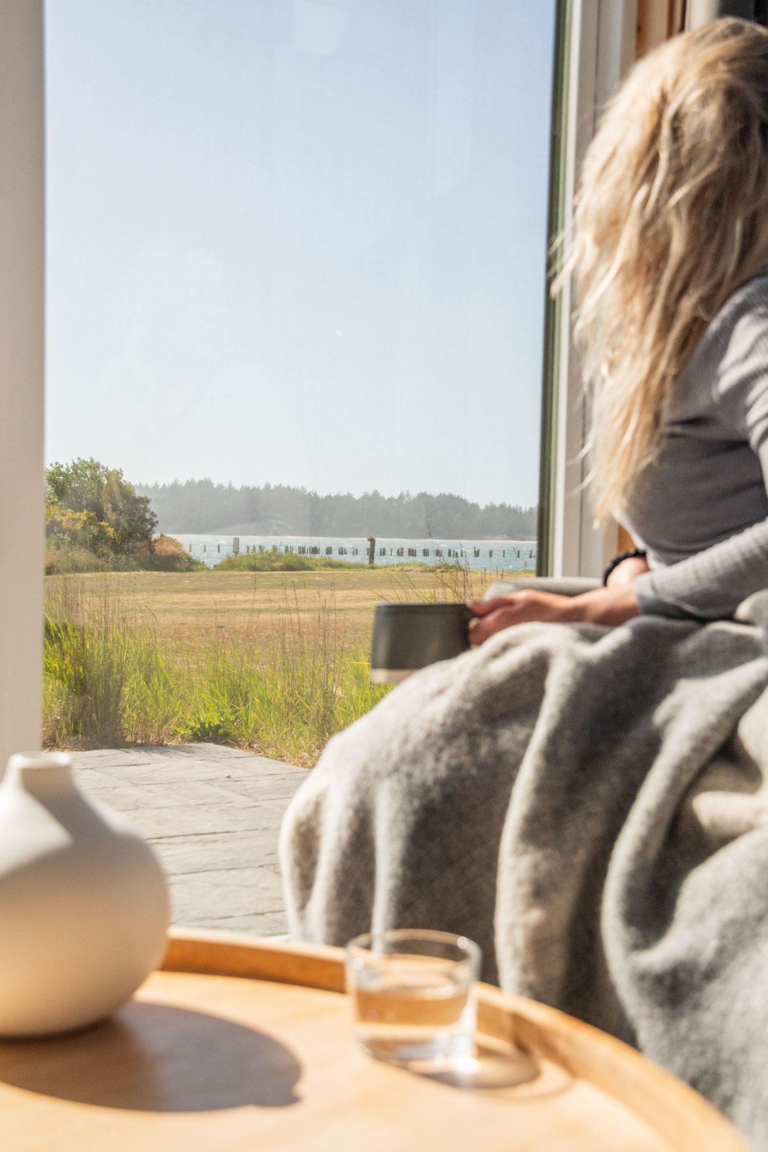 Cozy interior seating area with blanket overlooking coastal landscape through large windows.