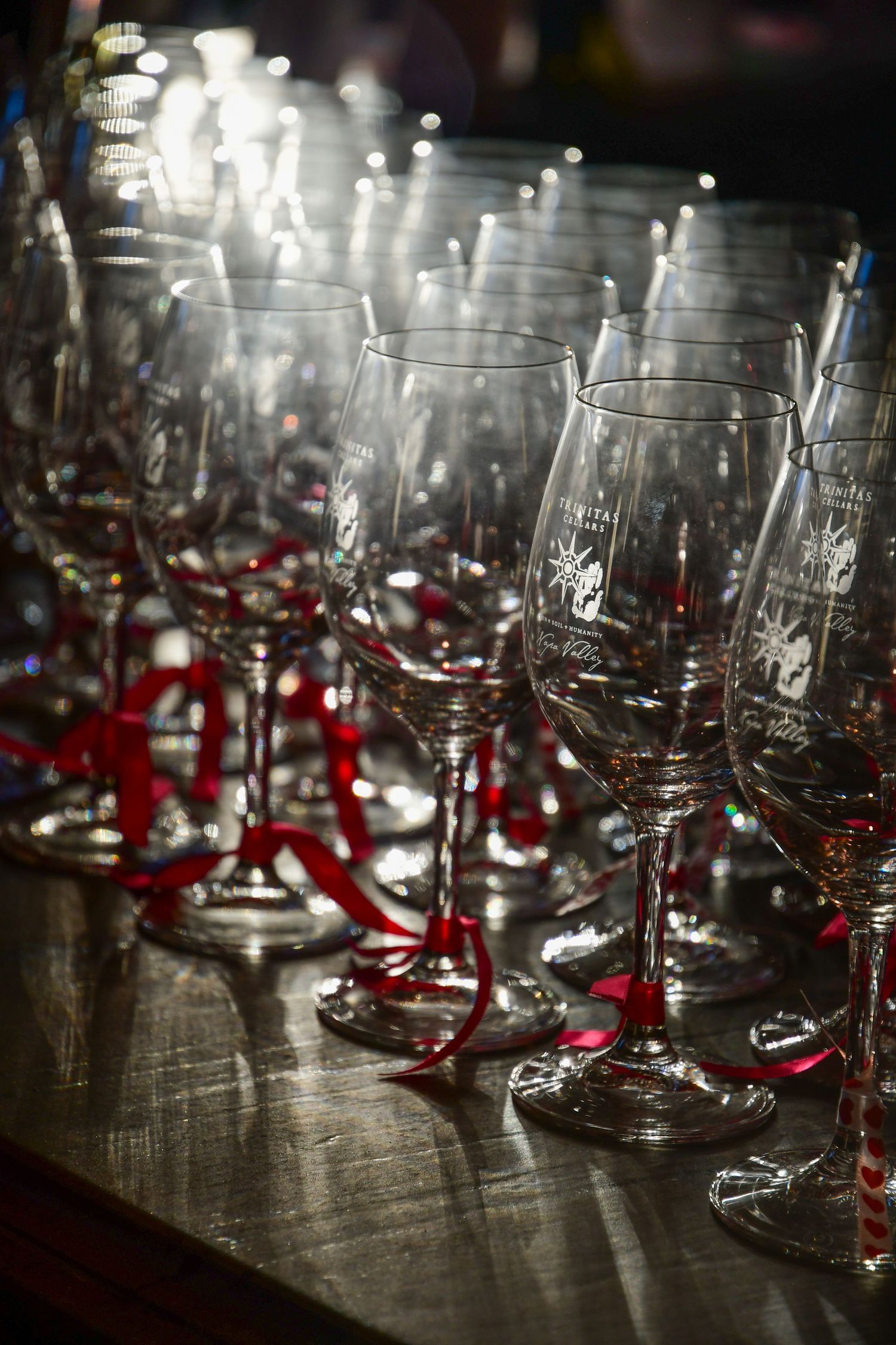 Empty wine glasses with red ribbons lined up on a dark wooden surface.