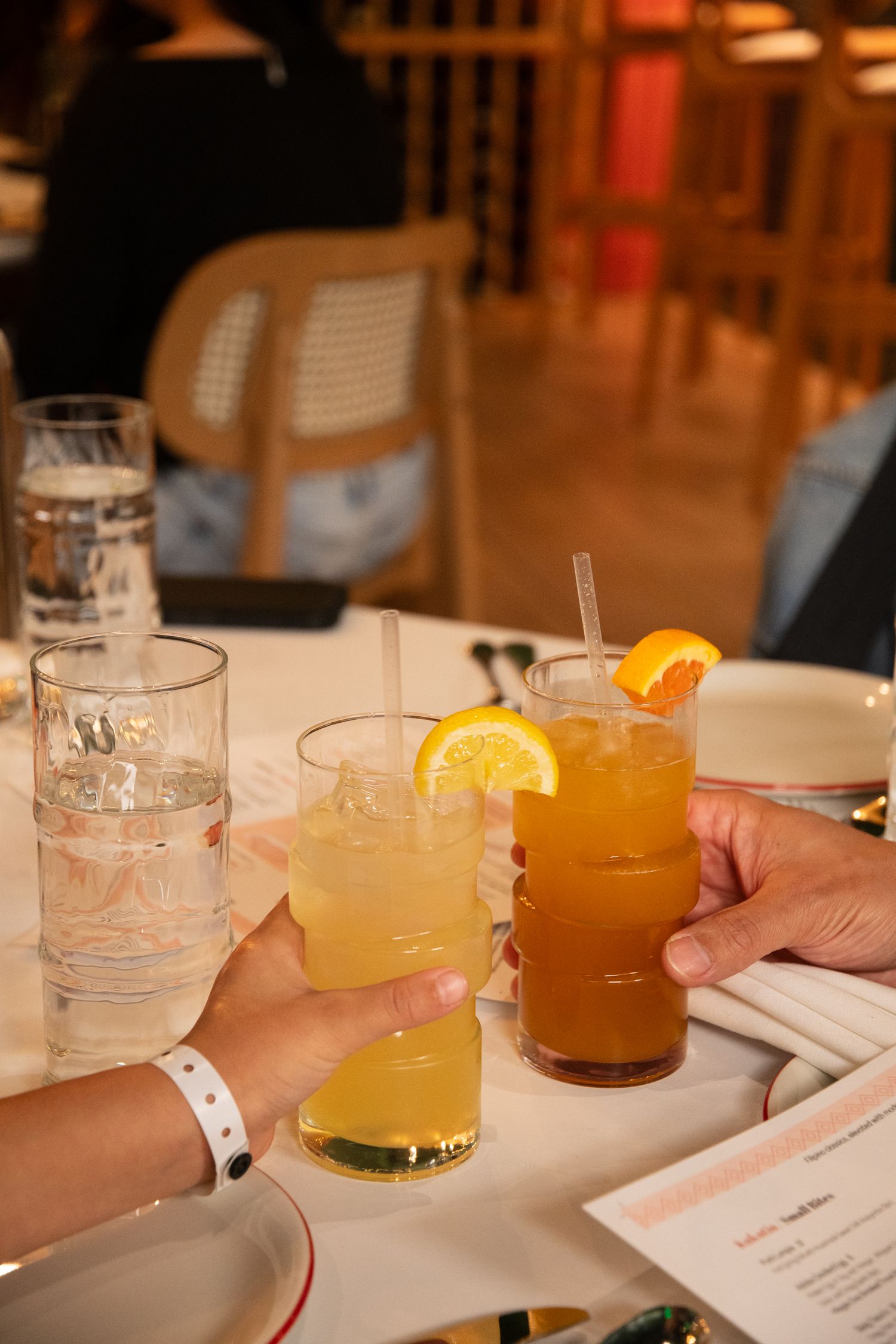 Lineup of colorful cocktails with citrus garnishes on a white tablecloth.