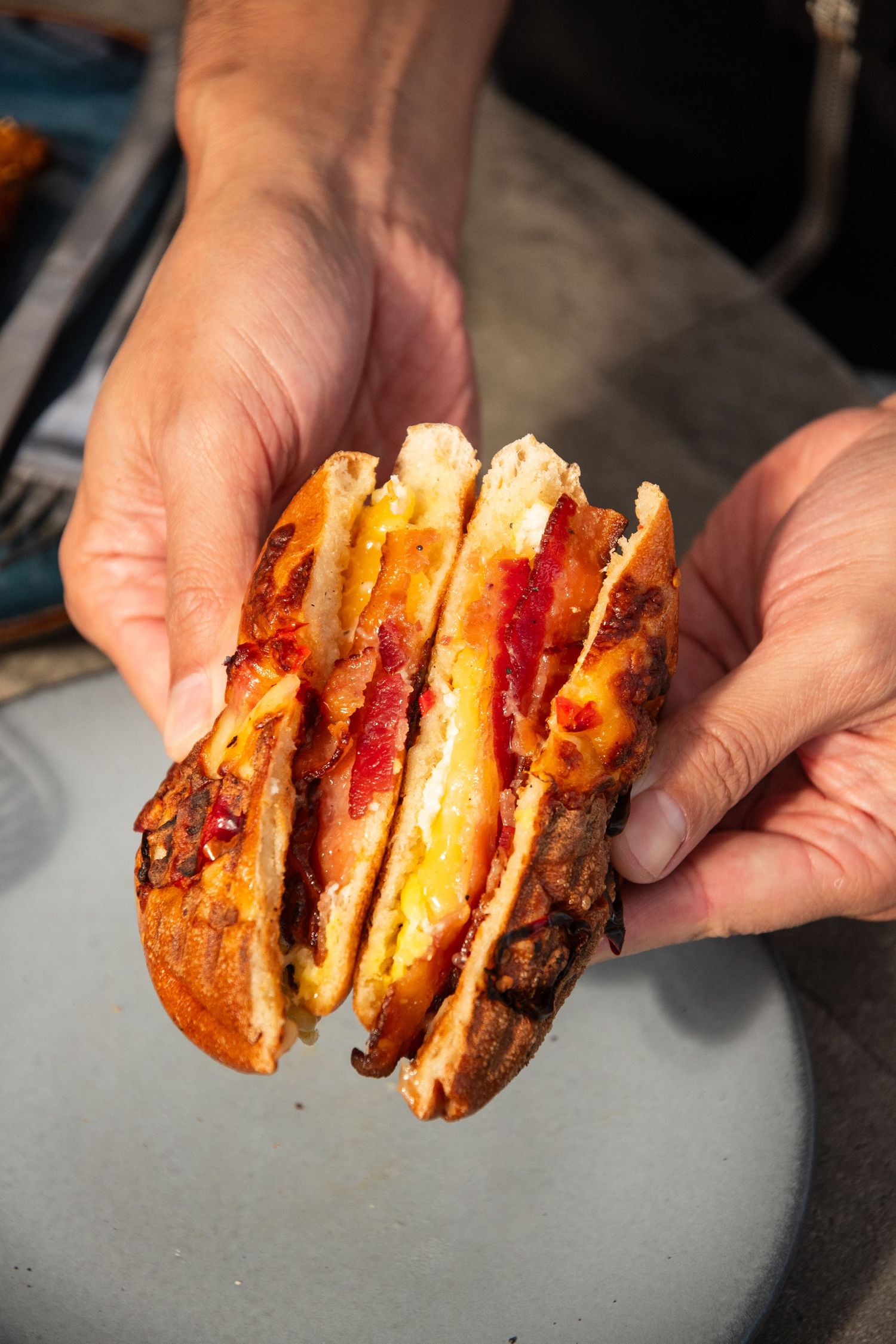Hands holding sliced pieces of grilled sandwich showing layers of melted cheese and filling.