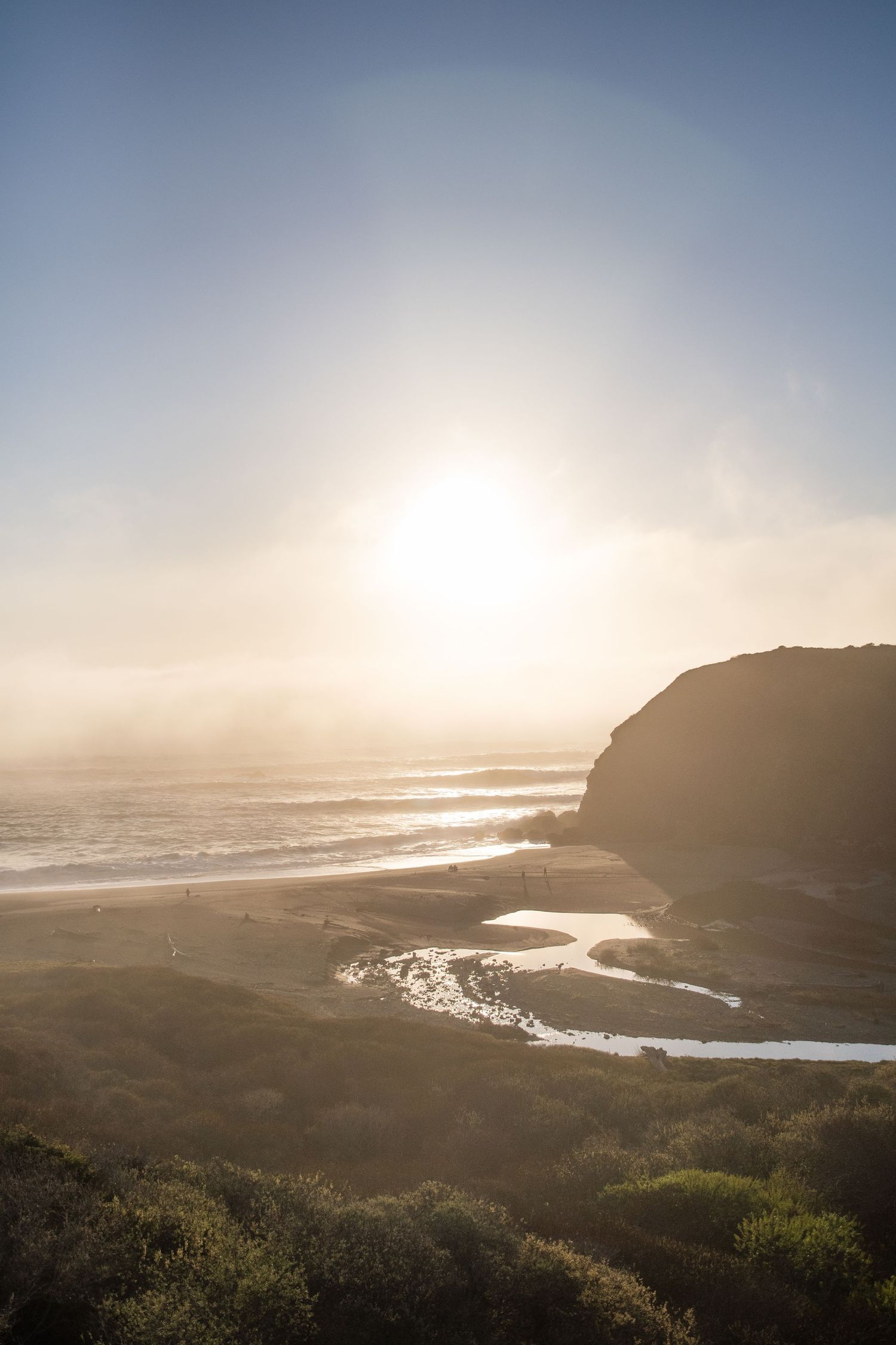 Dramatic coastal sunset over rocky cliffs with ocean waves breaking below.