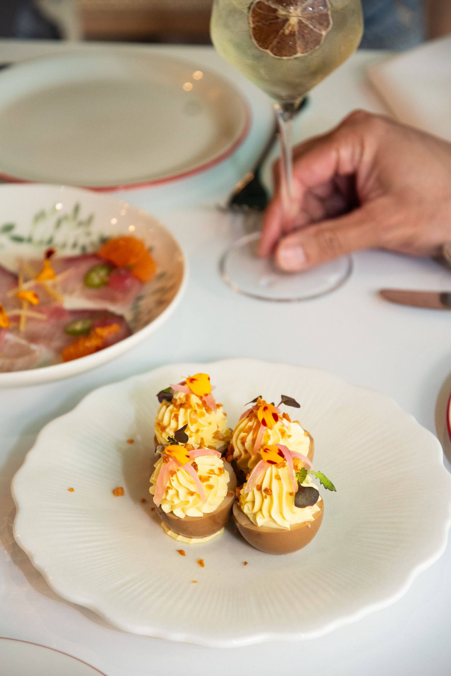 Deviled eggs garnished with colorful toppings and microgreens served on white plates at an upscale restaurant.