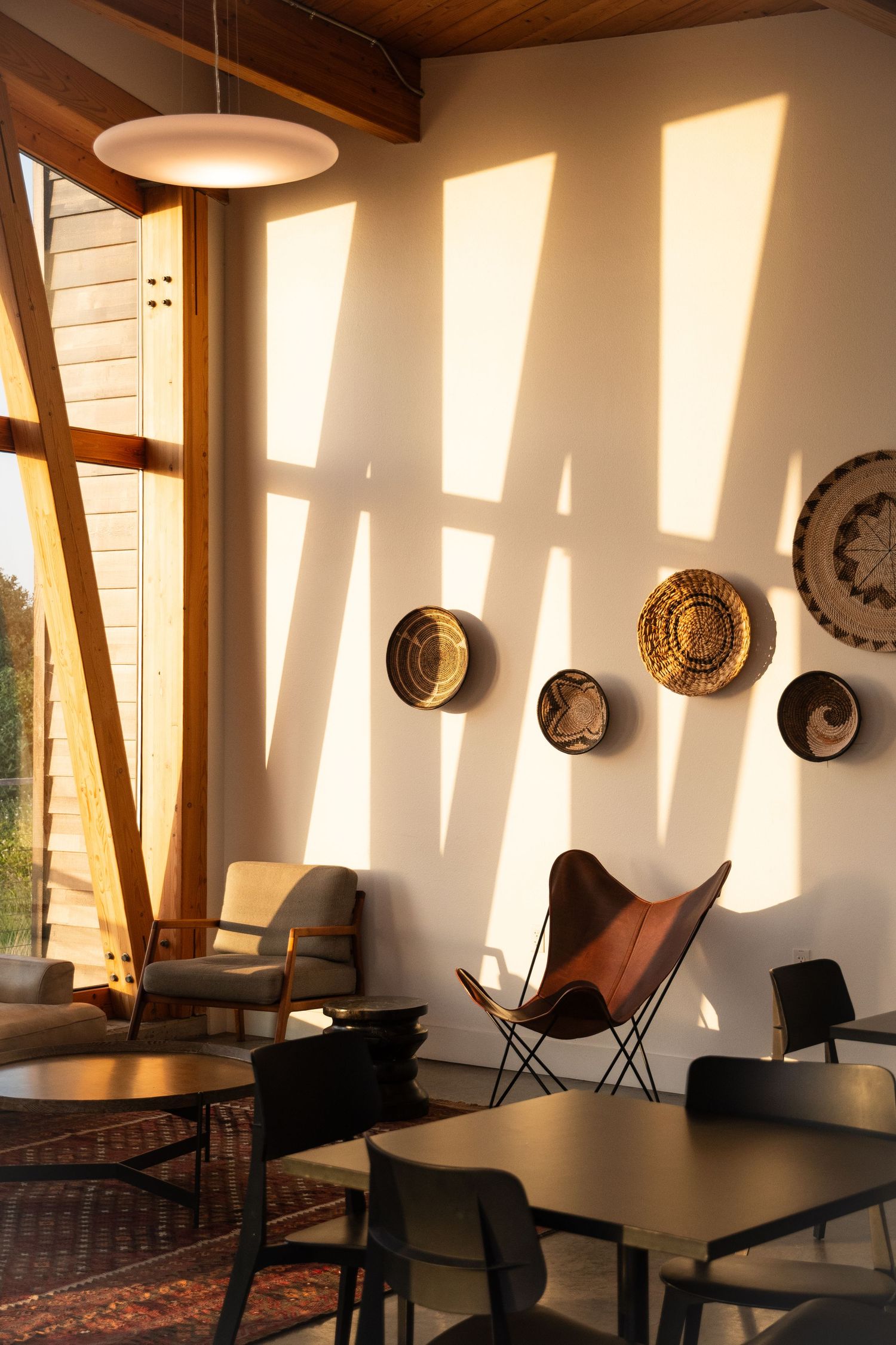 Modern living room with butterfly chairs and decorative wall baskets illuminated by dramatic sunlight.