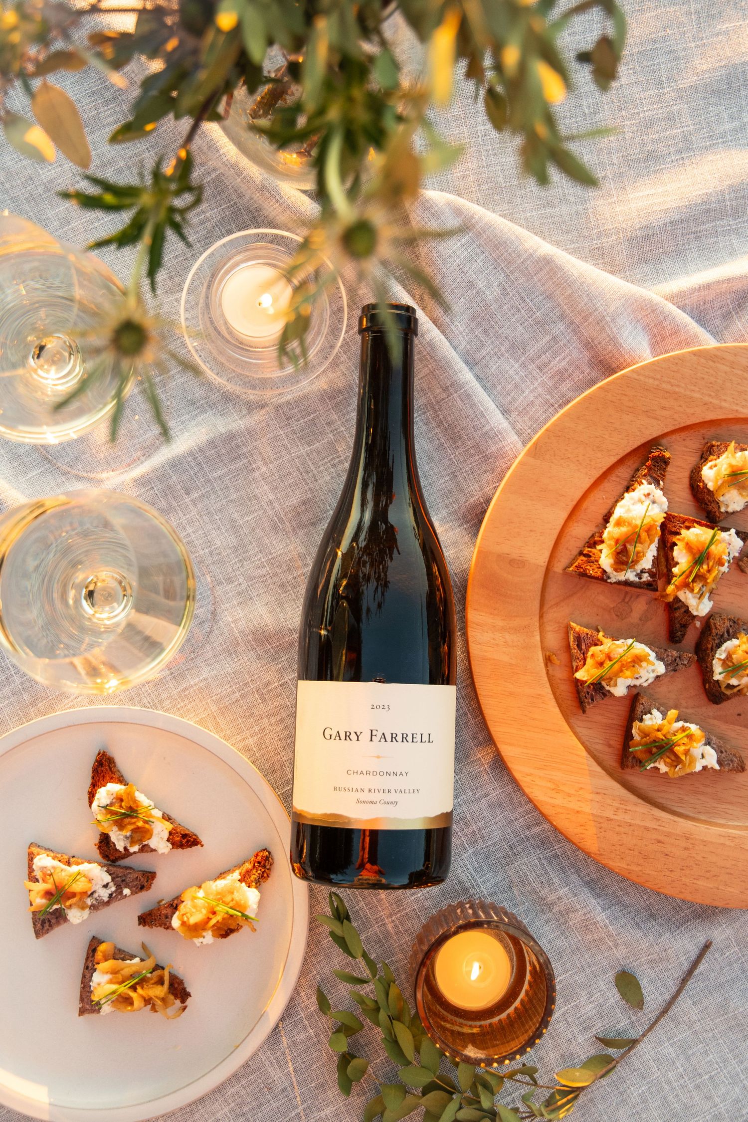 Wine bottle and appetizers arranged on a rustic wooden board with white plates and linens.
