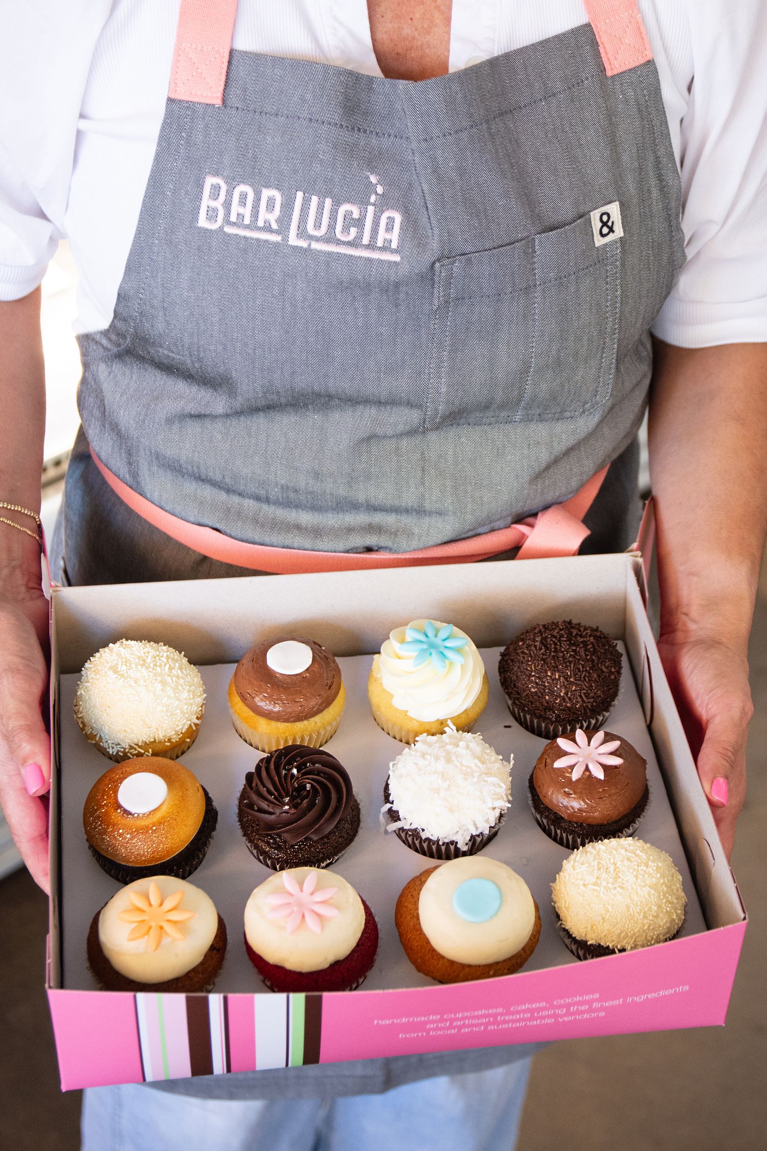 Display of artisanal cupcakes in pink box with Bar Lucia branding.