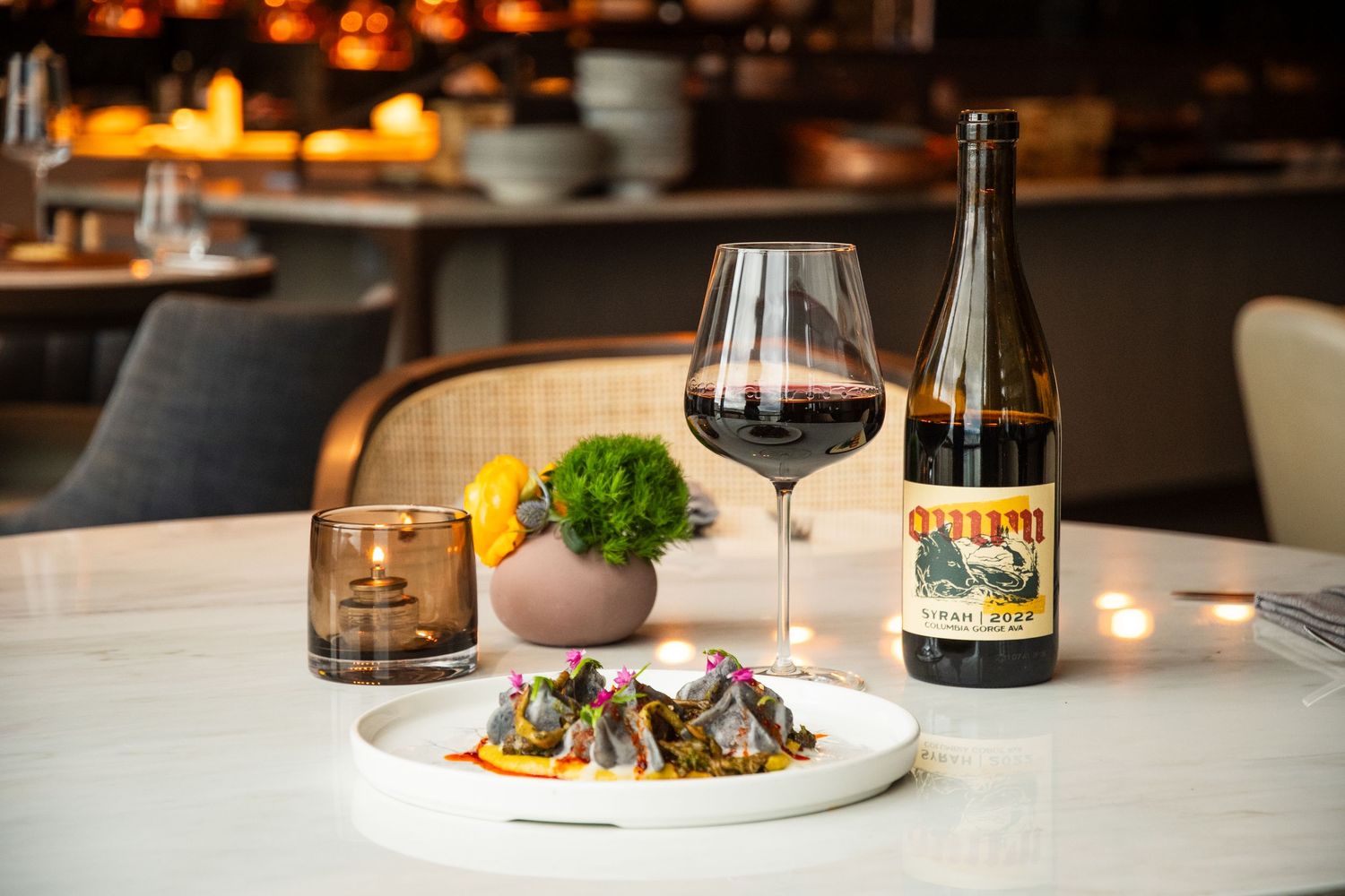 Elegant restaurant table with gourmet dish, red wine glass, and Pinot Noir bottle on marble surface.