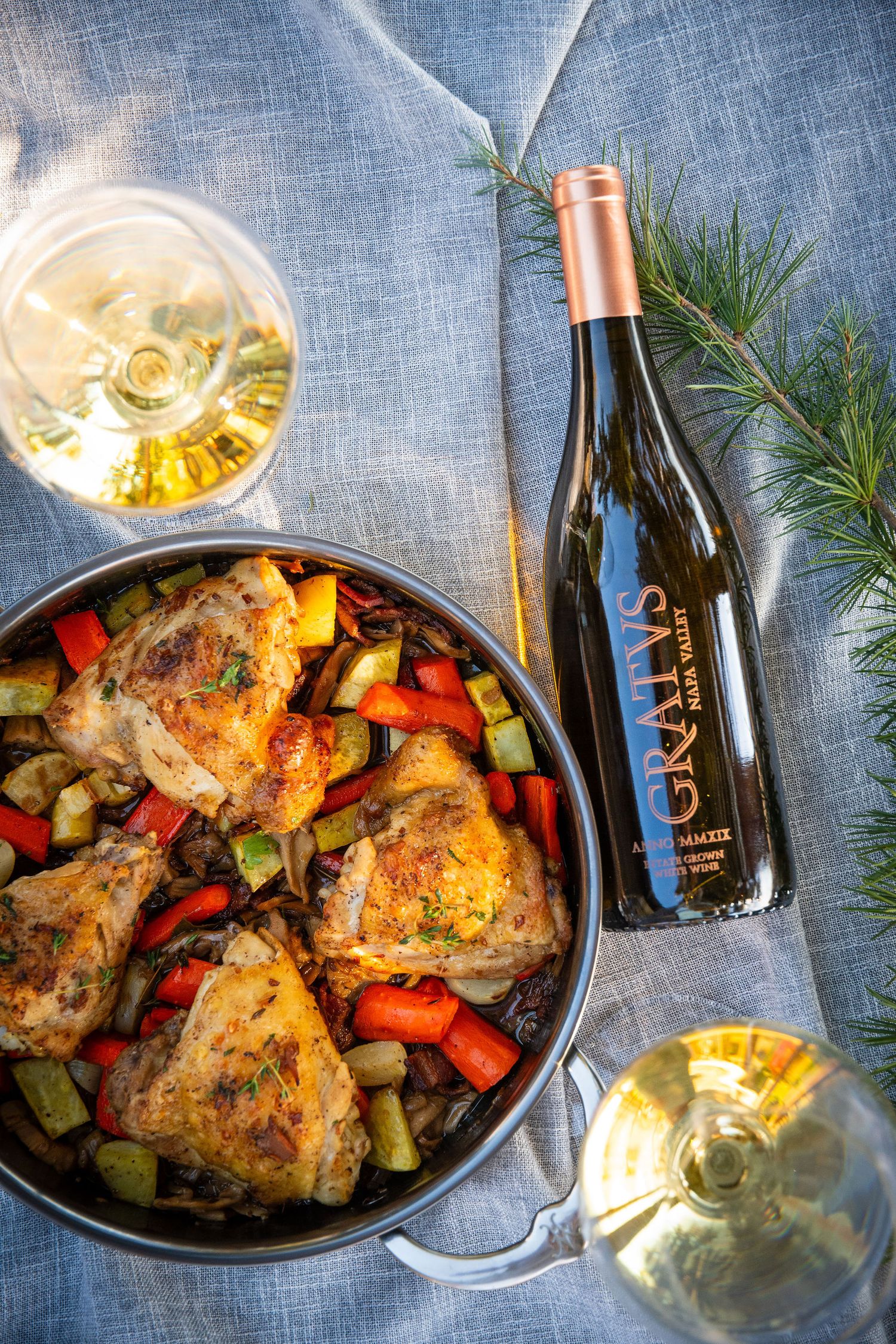 Rustic dinner setting with roasted chicken and wine bottles on blue linen tablecloth.