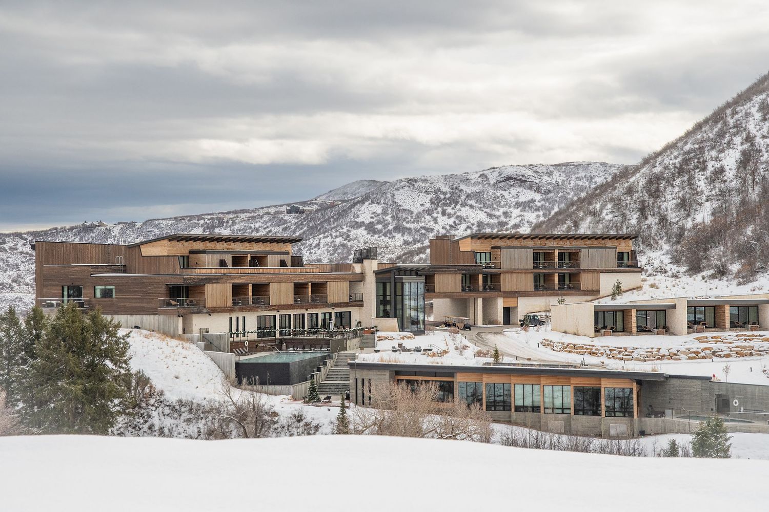 Modern mountain resort buildings nestled in snowy landscape under cloudy skies.