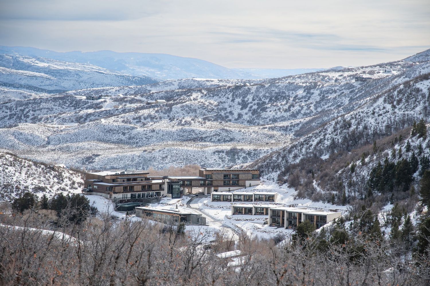 Snow-covered mountain resort with modern multi-level architecture nestled in a winter valley landscape.