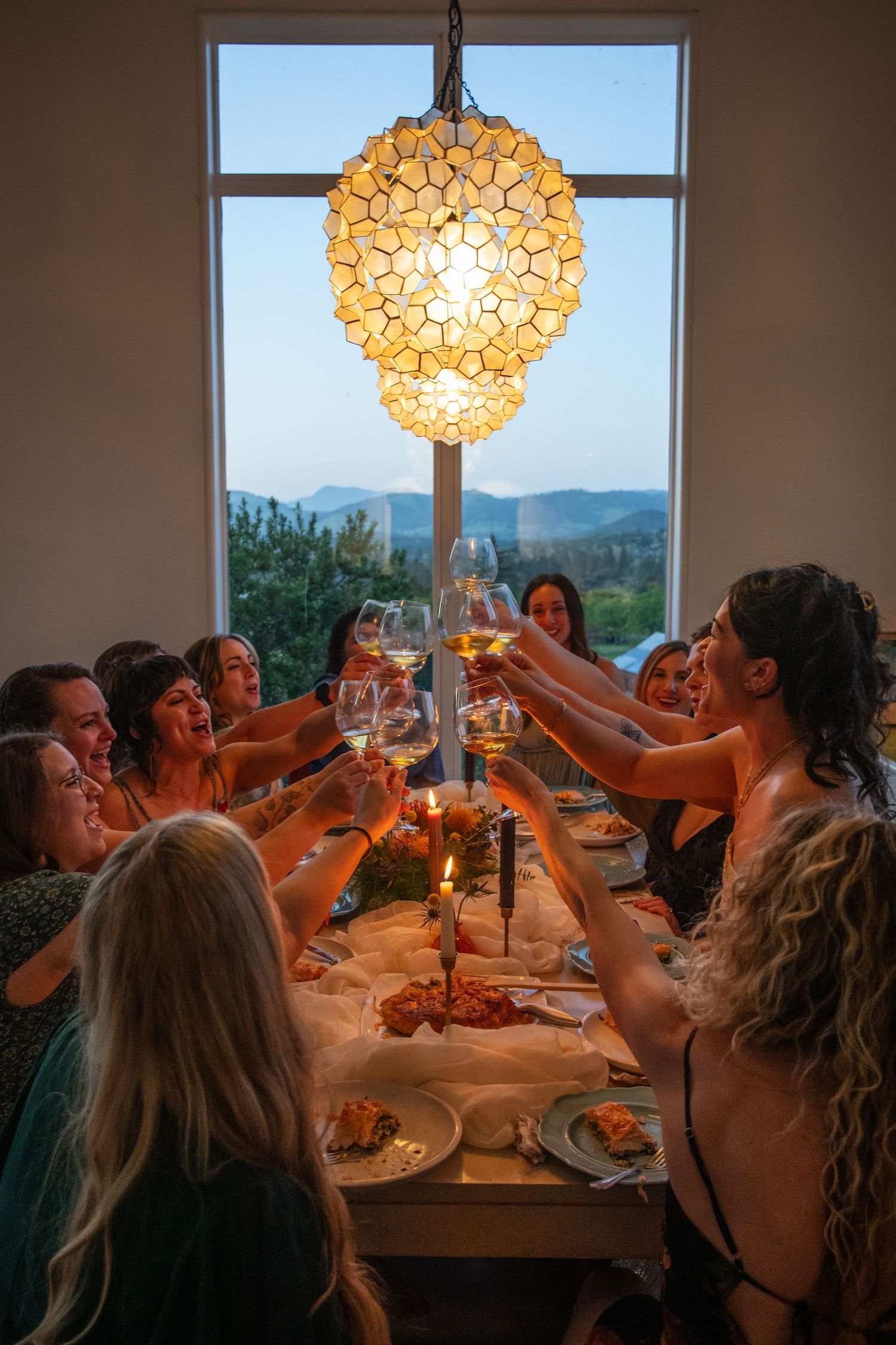 Dinner gathering with wine toasts under a decorative capiz shell chandelier with mountain views.